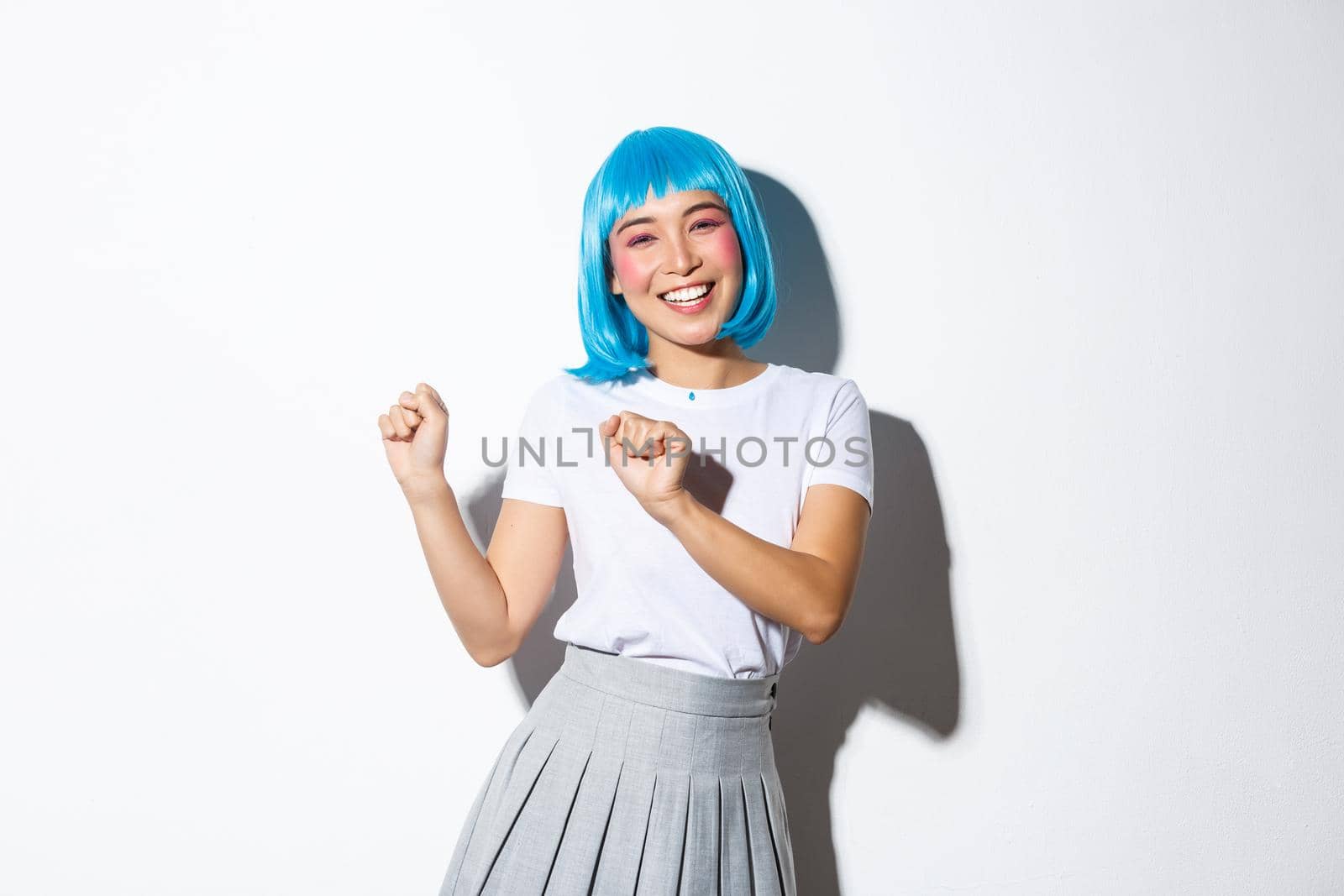 Portrait of attractive asian girl in blue wig dancing and having fun, partying, wearing halloween costume and celebrating, smiling at camera.