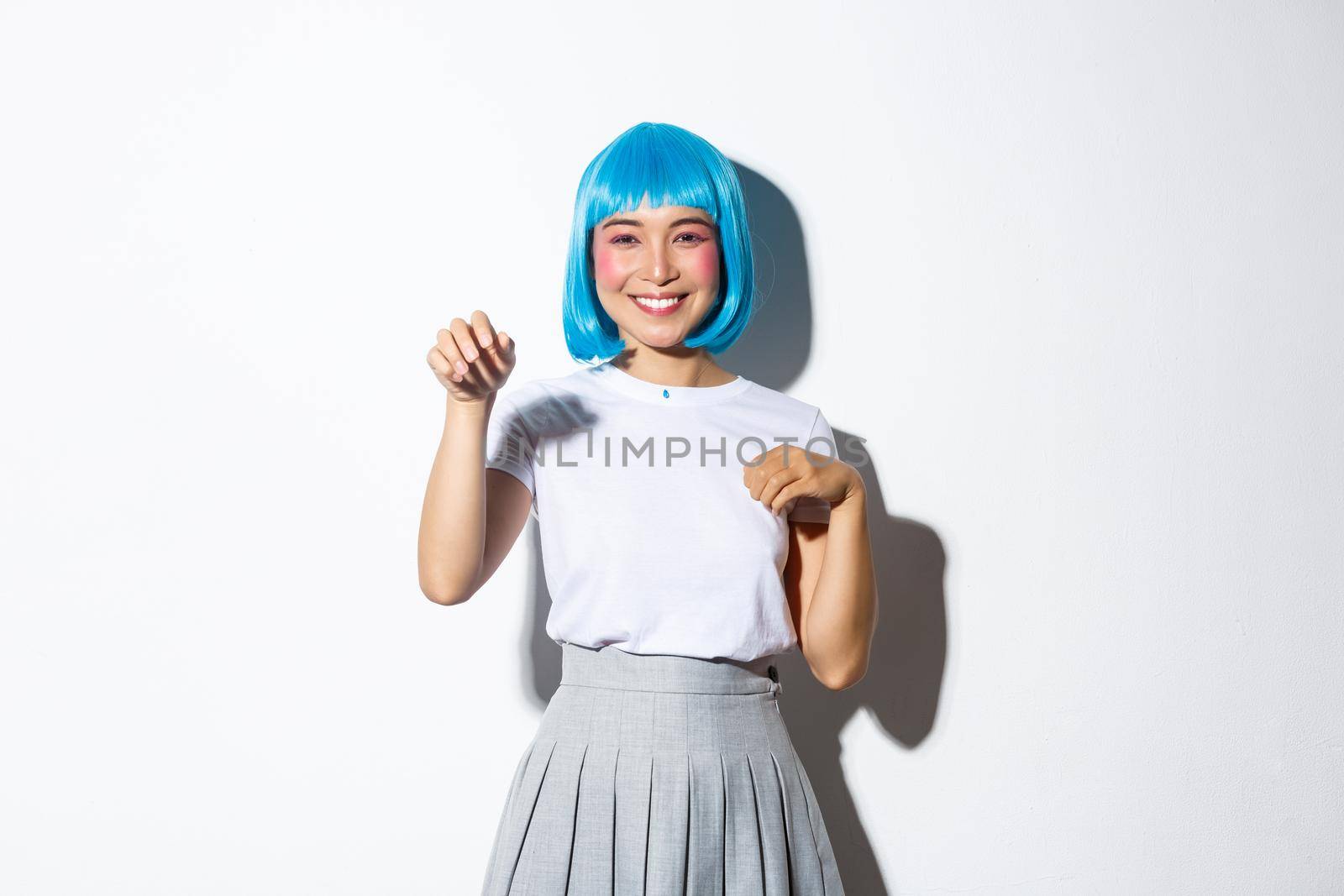 Portrait of funny and cute korean girl in blue wig celebrating halloween, waving hand like a paw, standing over white background.