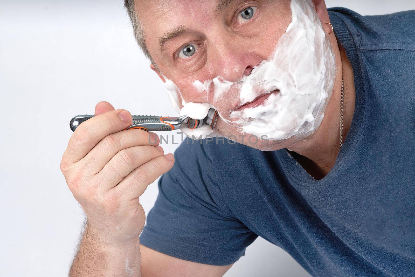 A man's face in shaving foam shaves with a safety razor. Morning or evening exercise, personal hygiene