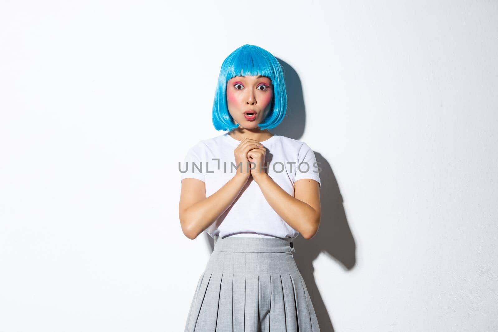 Portrait of surprised asian girl in blue short wig gasping amazed, hear something shocking, standing in halloween costume over white background by Benzoix
