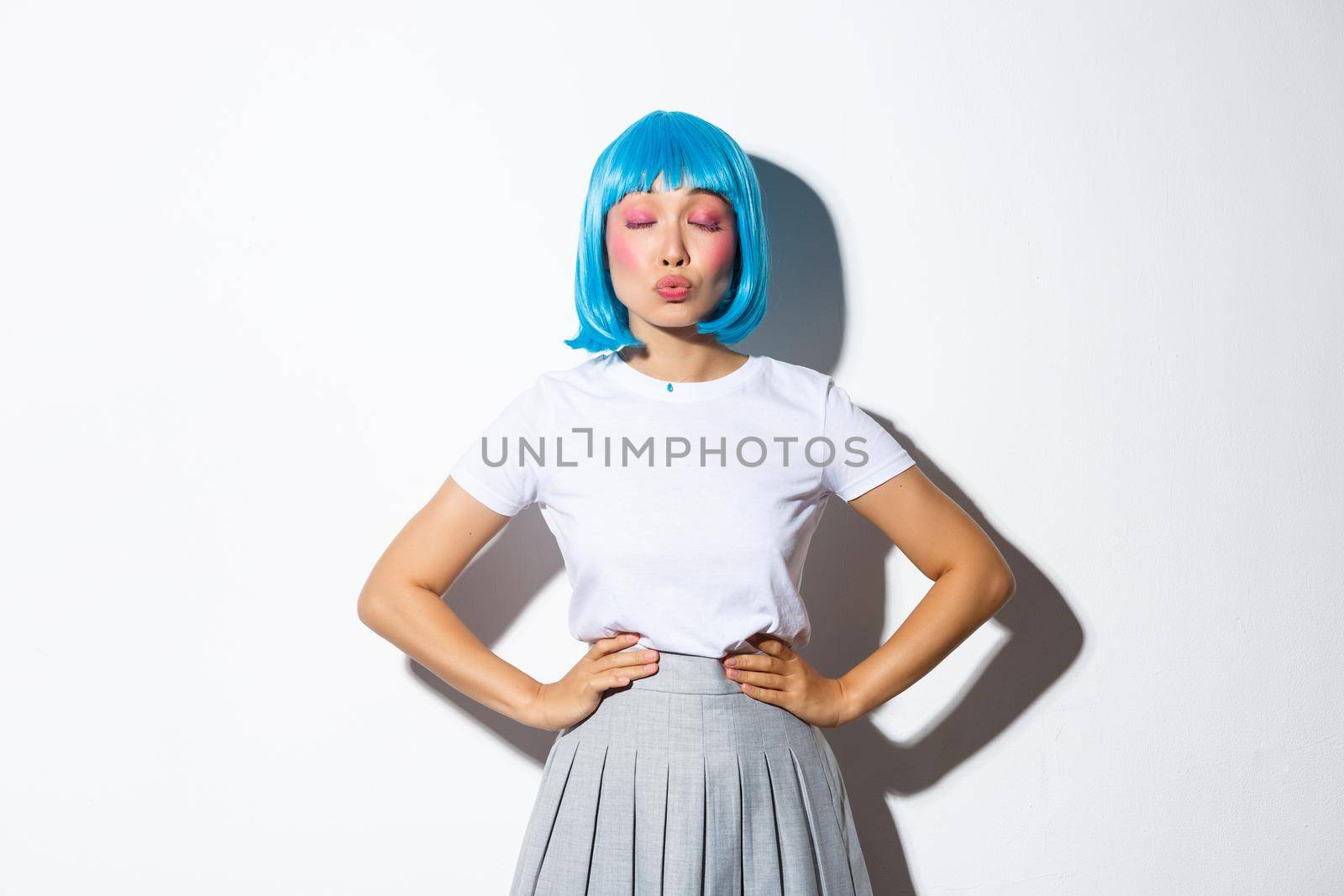 Portrait of lovely cute asian girl, close eyes and pouting for kiss, wearing blue wig and schoolgirl costume, standing over white background.