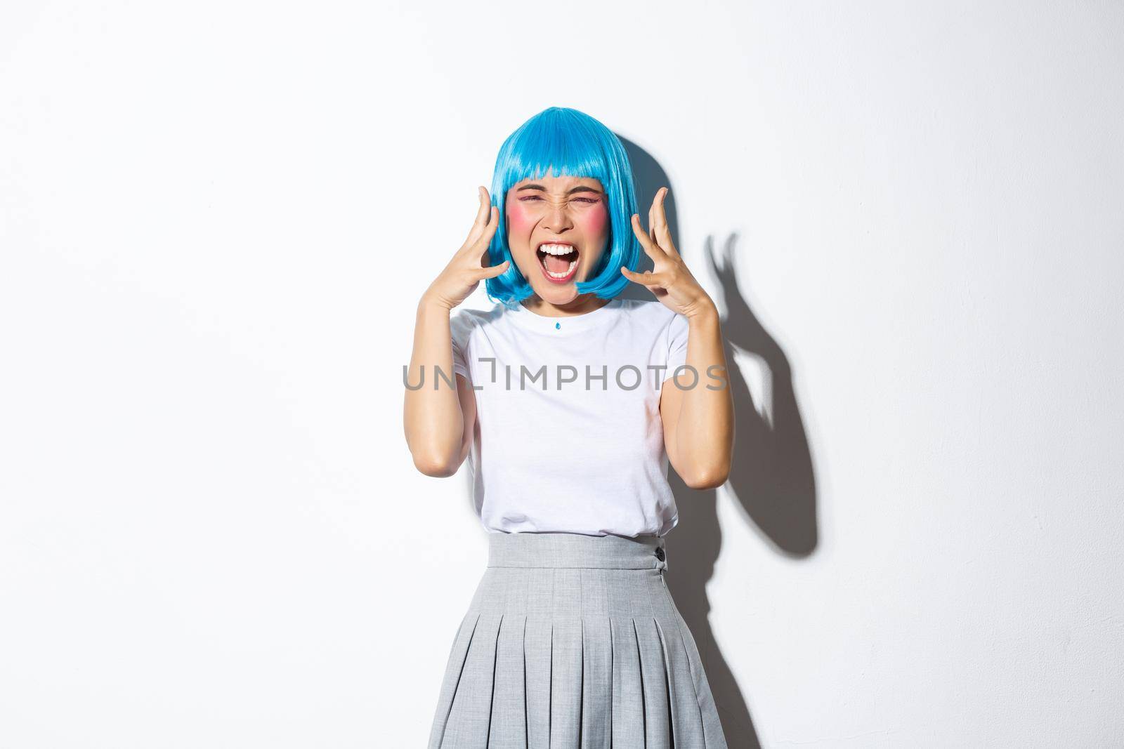 Portrait of distressed mad asian girl in blue wig screaming angry, standing over white background by Benzoix