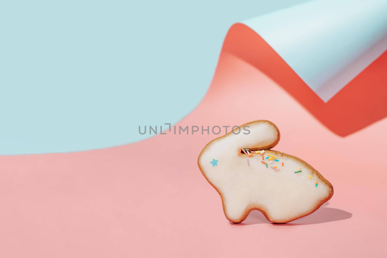 Easter bunny cookie on pink and blue curved paper pastel background with shadows. Happy Easter Day concept. Minimal Easter concept. Copy space for text. Easter cooking baking background.
