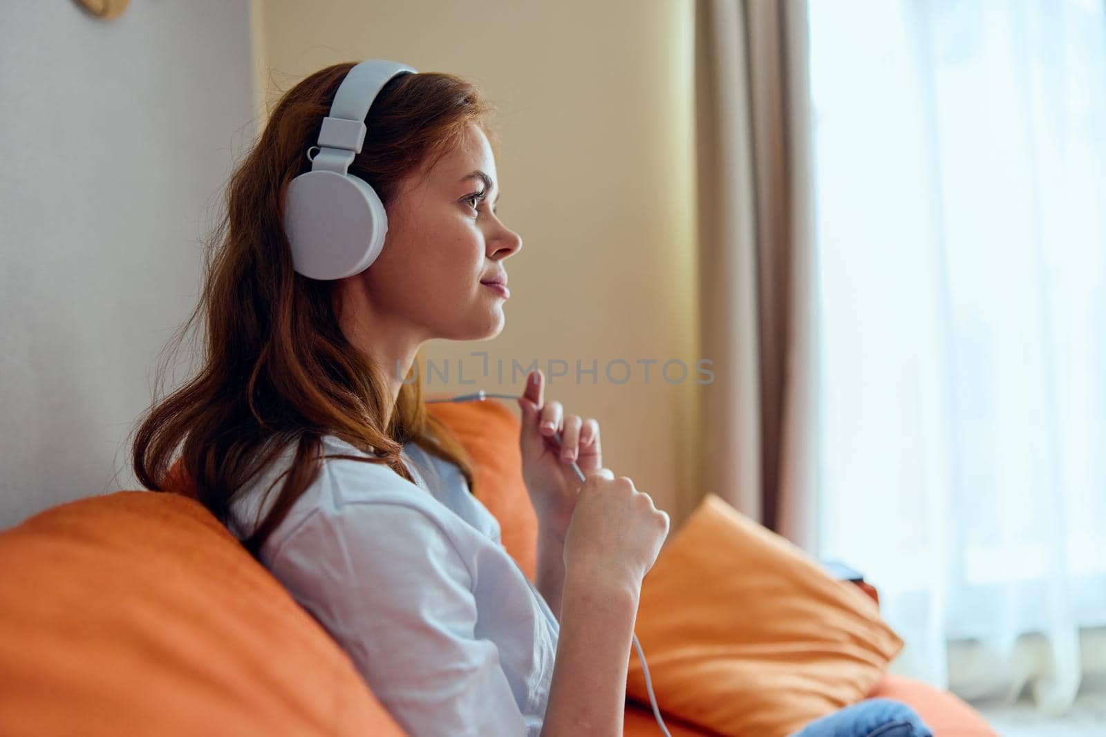 cheerful woman listening to music with headphones on the orange sofa technologies. High quality photo