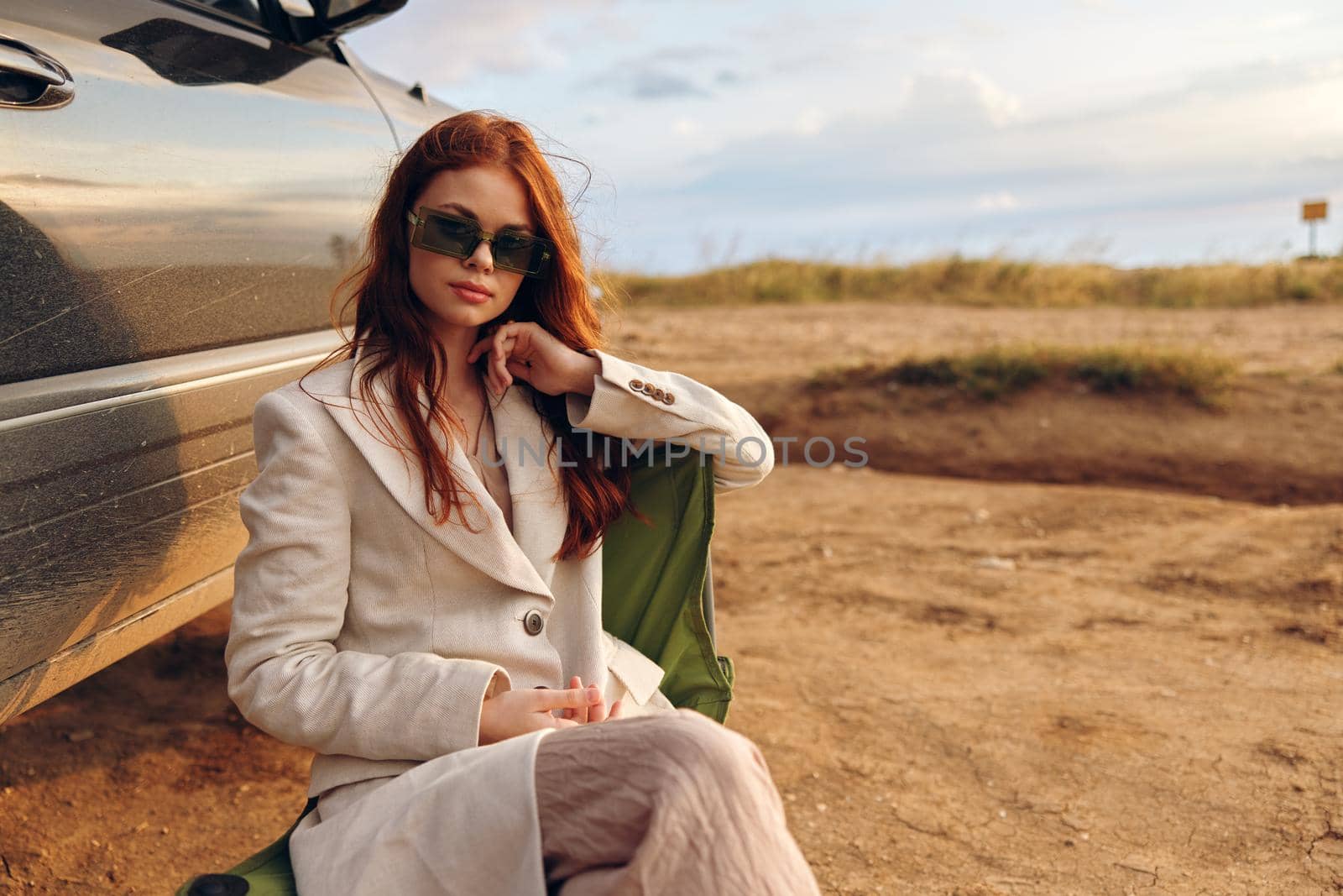 beautiful woman in a coat outdoors sitting on a chair near the car autumn season concept. High quality photo