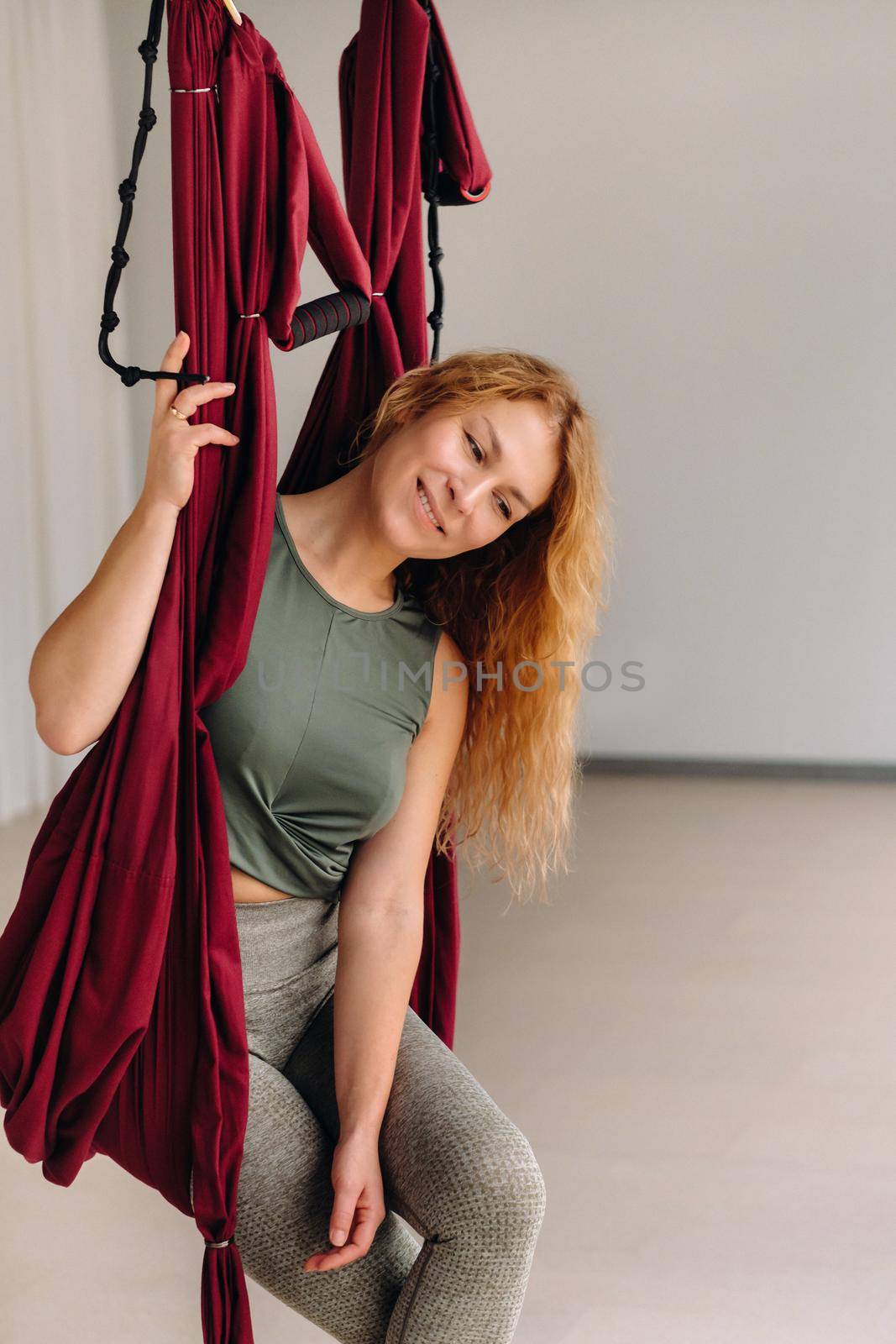 A woman does yoga sitting in a hanging hammock in the gym.