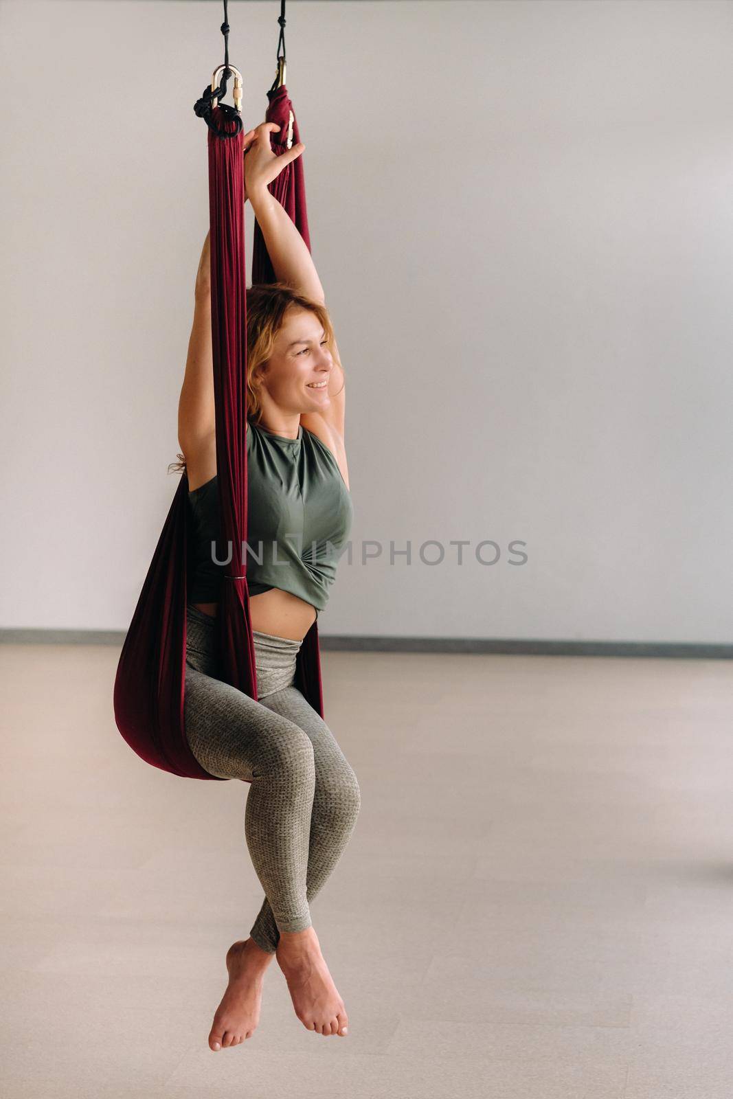 A woman does yoga sitting in a hanging hammock in the gym.