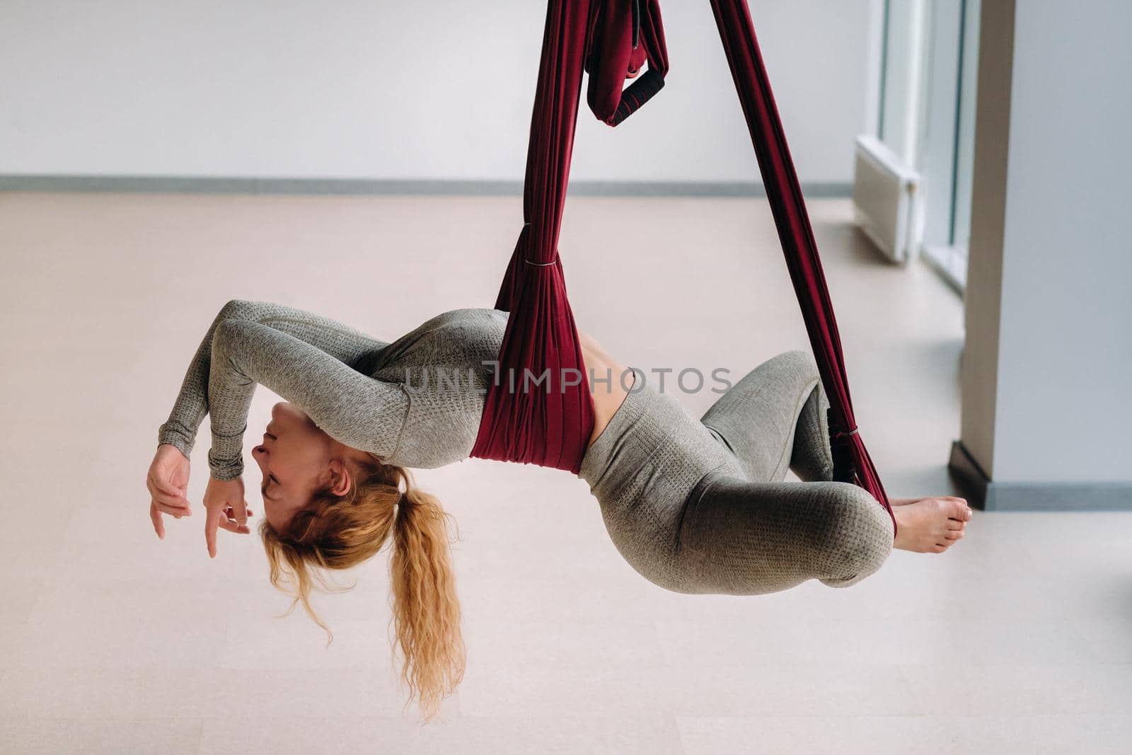 A woman hanging on a hanging hammock does yoga in the gym.