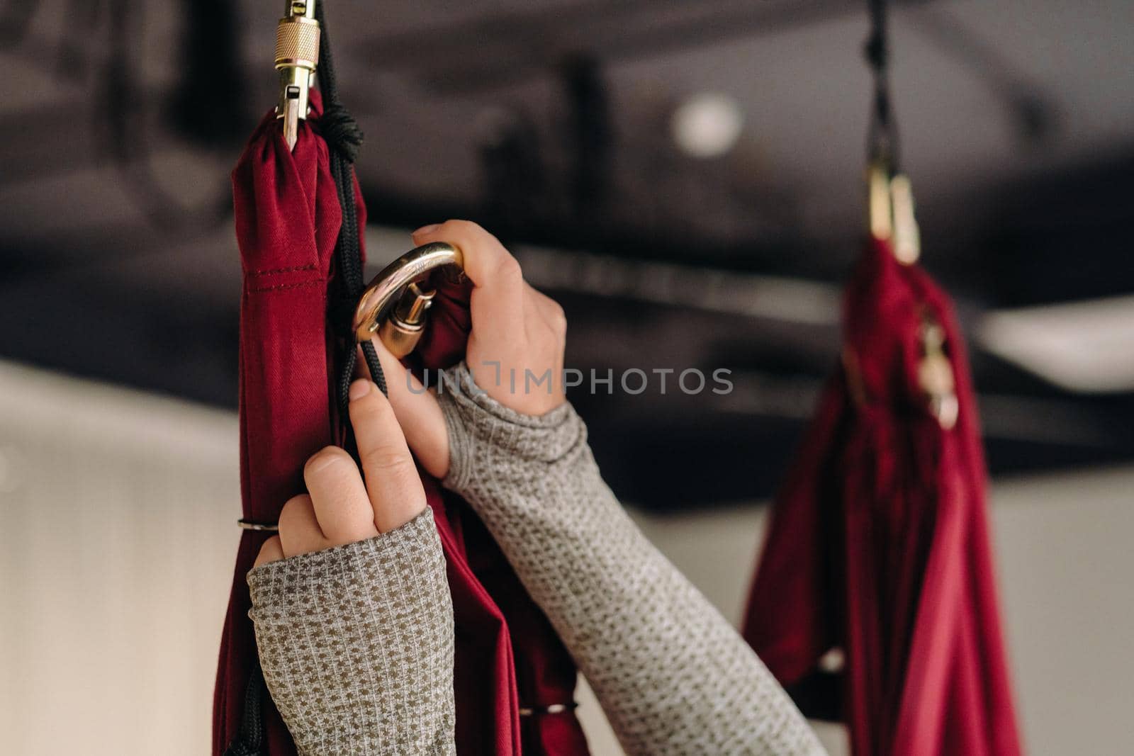 close-up of a girl's hands fastening a hook to a hanging hammock for yoga classes in the gym.