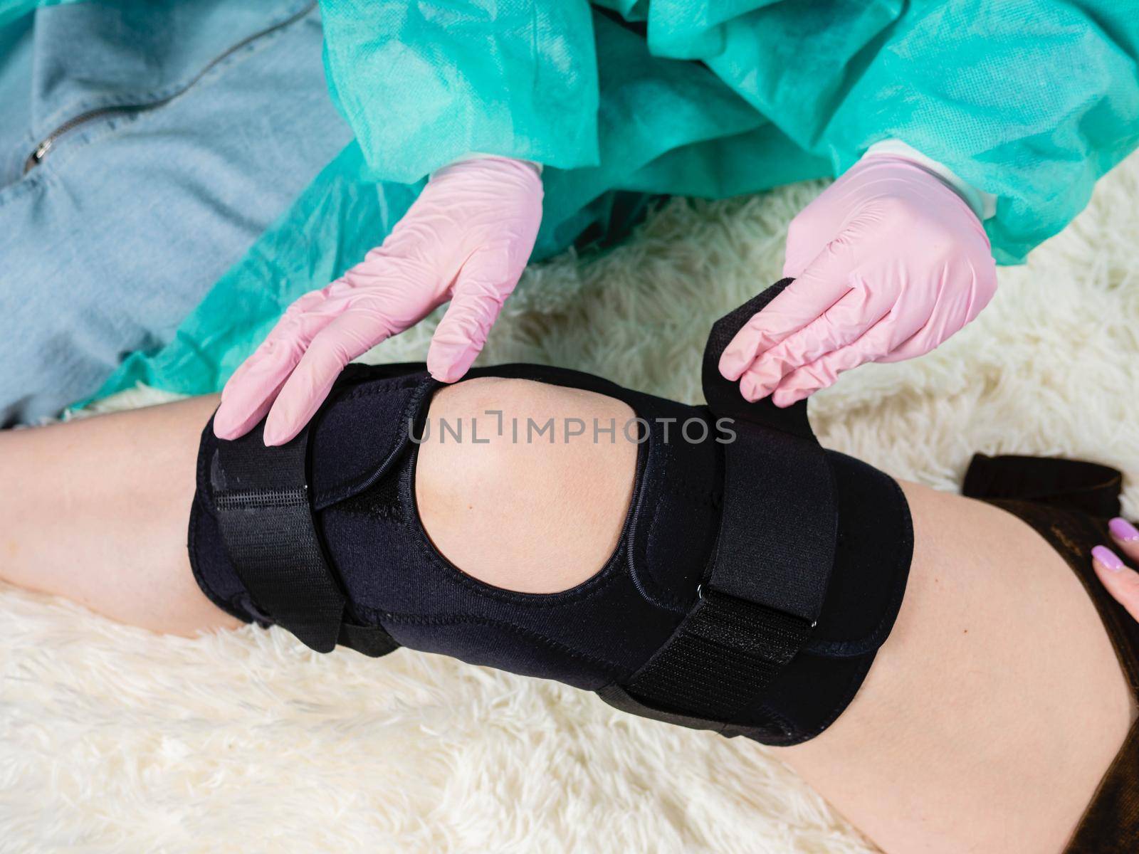 close-up of a family doctor putting a black brace on a patient's knee by Utlanov