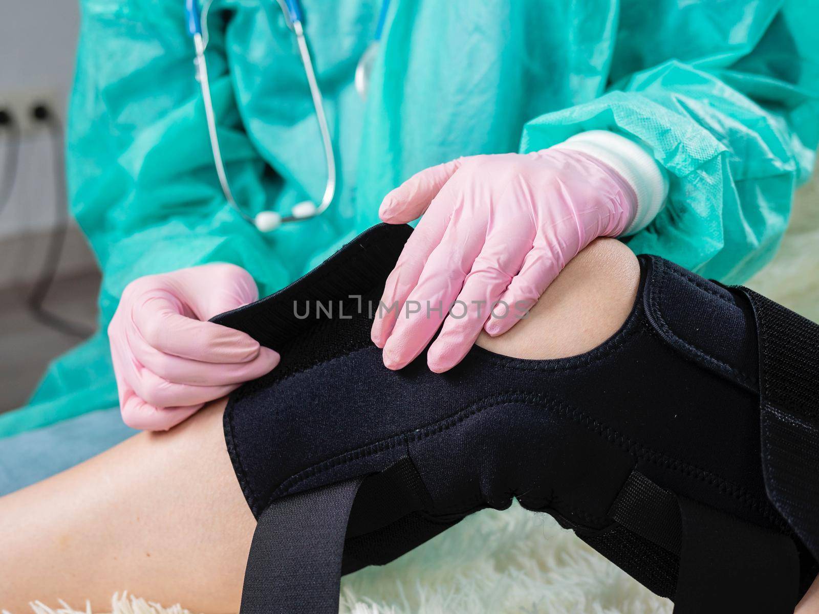 Close-up of the hand of a physiotherapist who helps a patient with a knee brace orthosis after an injury