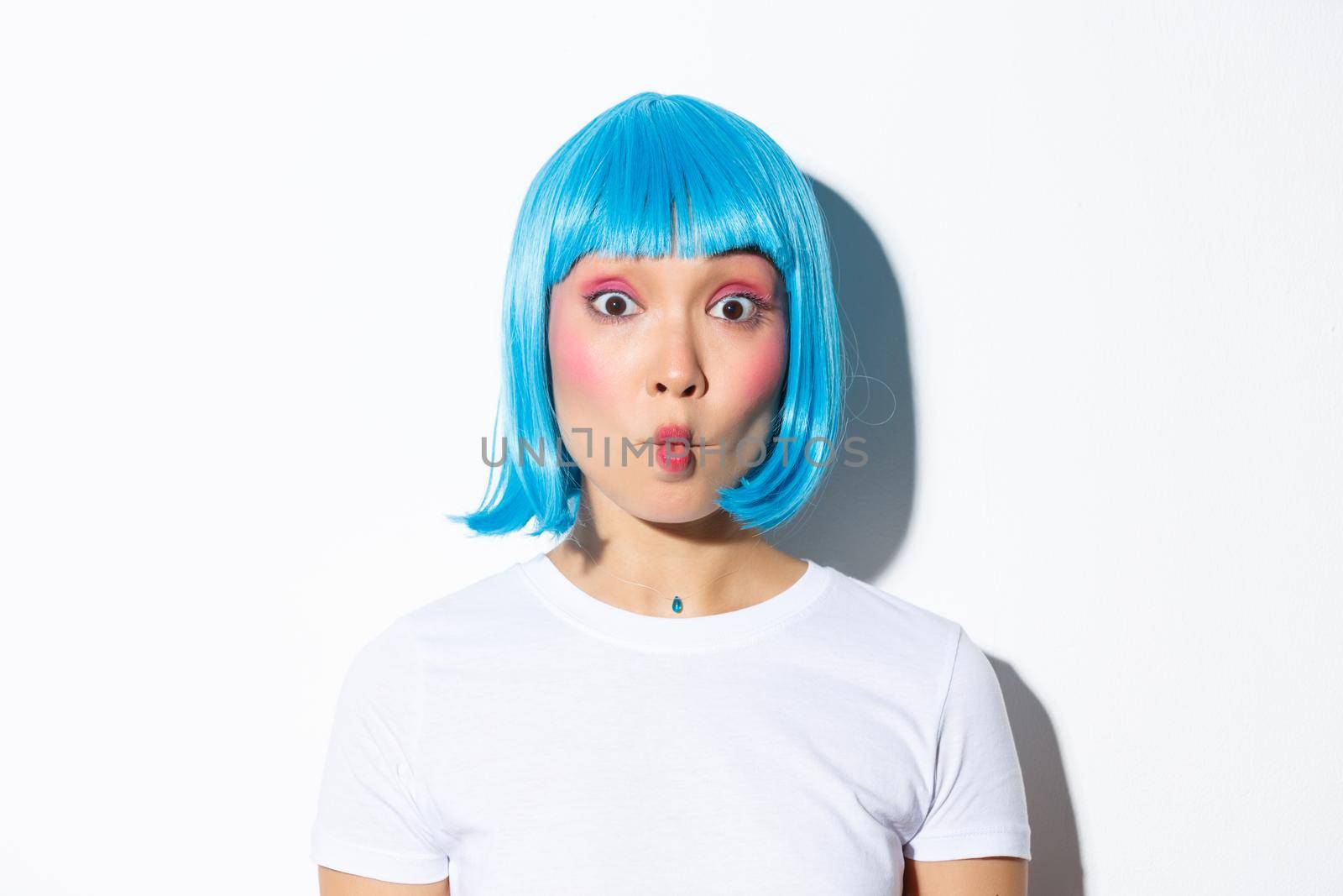 Close-up of funny and silly asian girl entertainer celebrating halloween, wearing blue wig, showing grimaces.