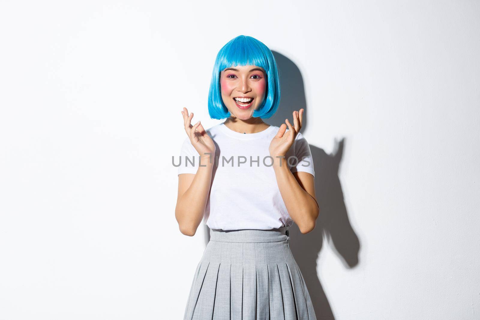 Portrait of happy attractive asian girl in blue shirt wig clap hands, applause and smile at camera. Woman in halloween costume standing over white background by Benzoix