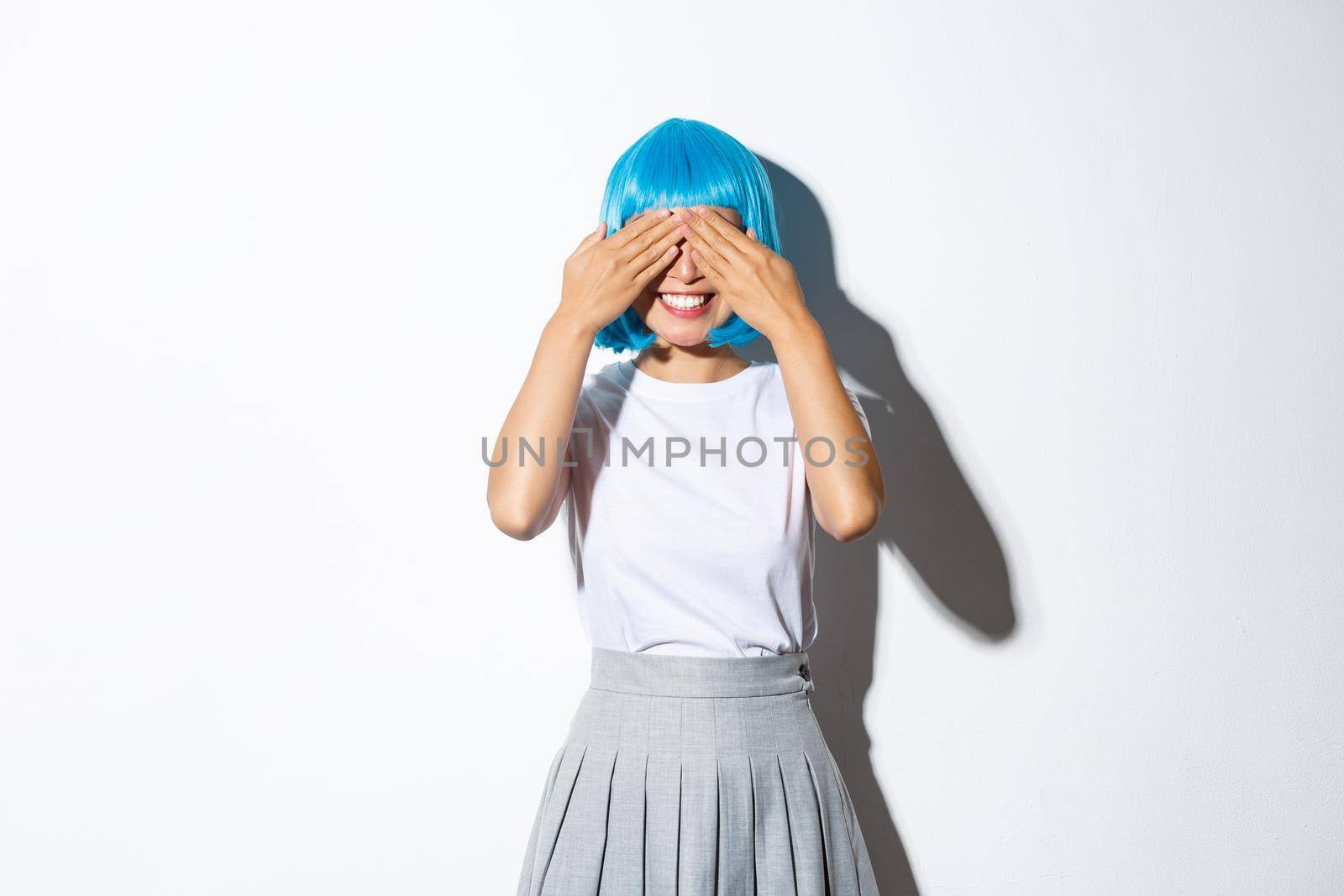 Portrait of dreamy cute asian girl in blue wig close her eyes with hands and smiling, waiting for surprise, celebrating halloween at party by Benzoix