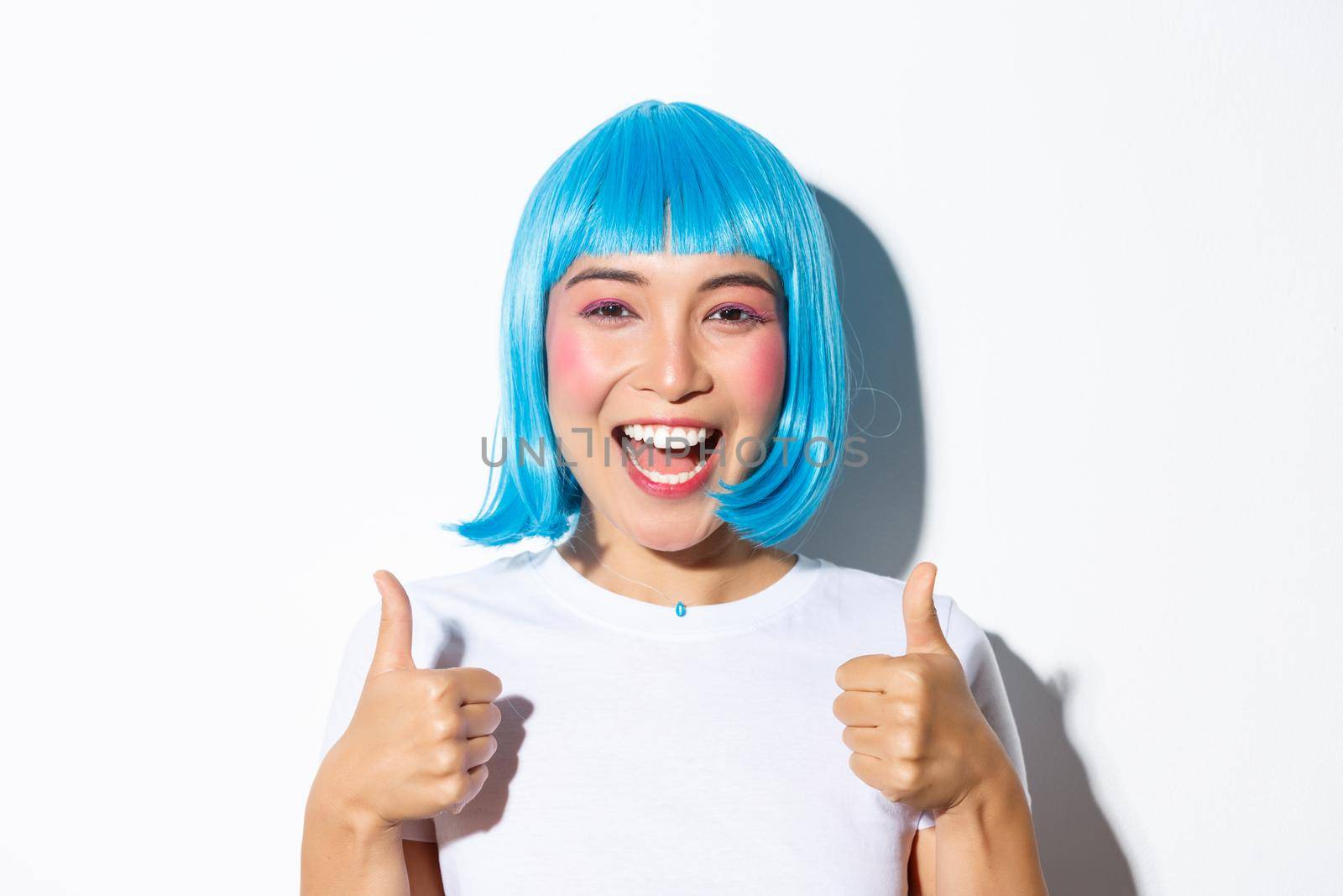 Portrait of happy smiling girl in blue wig, showing thumbs-up in approval.