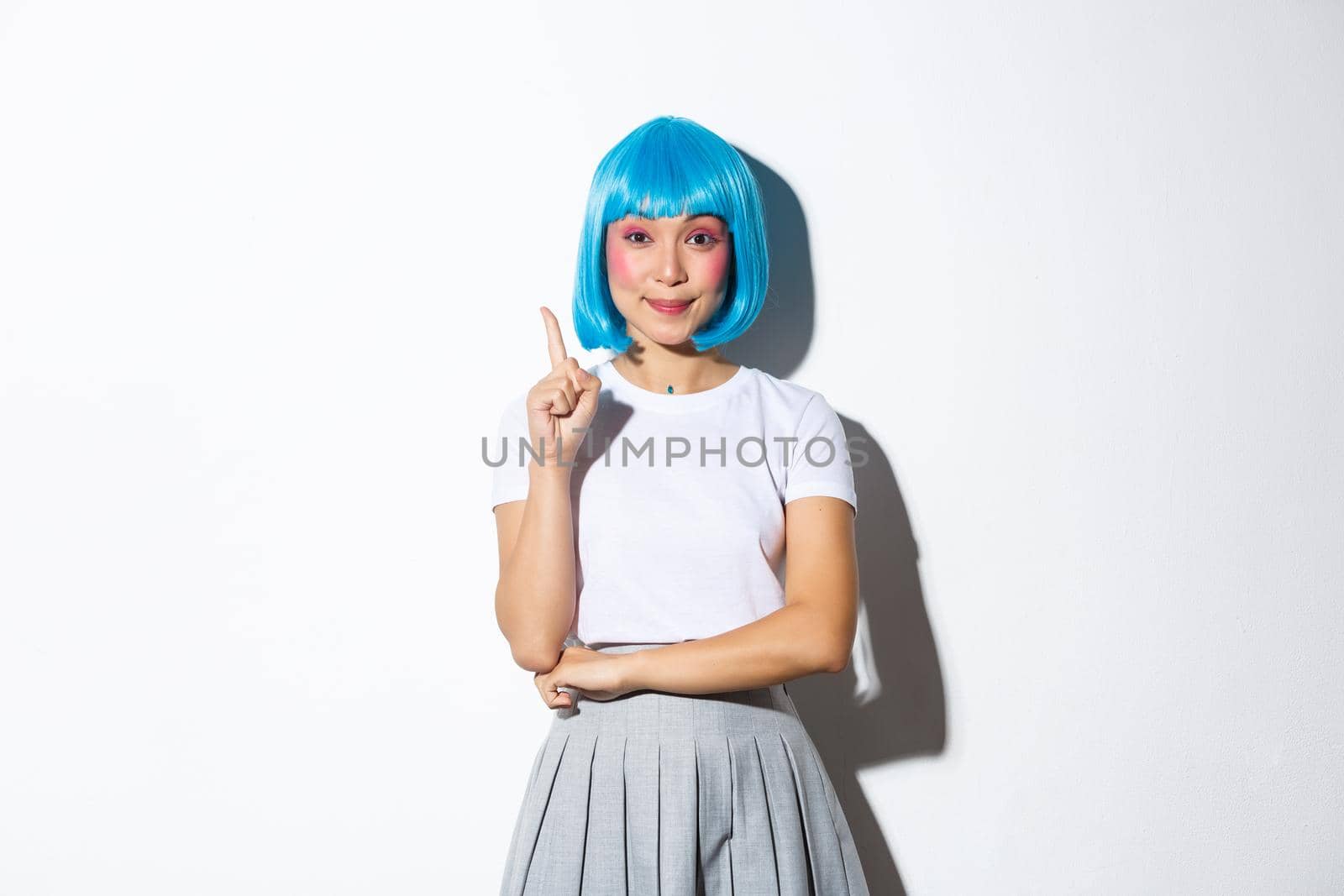Portrait of smiling confident asian girl in blue wig and halloween costume having solution, raising finger in eureka gesture, standing over white background.