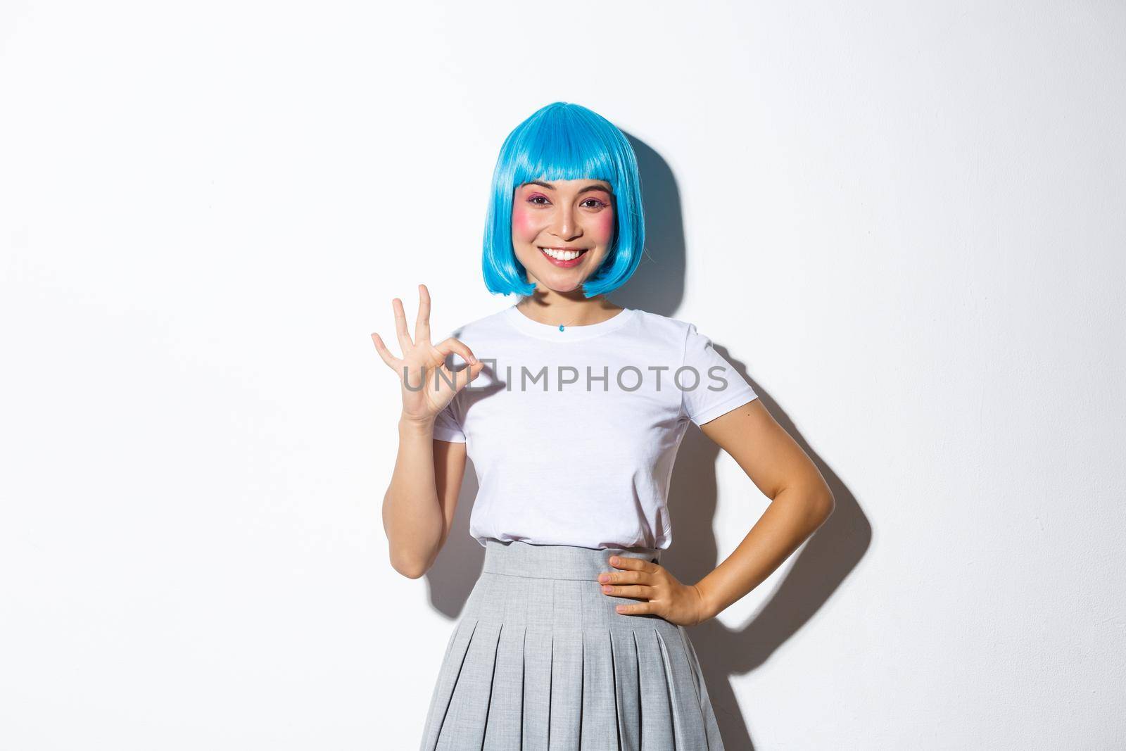 Portrait of smiling beautiful asian girl showing okay gesture in approval, recommend something good, standing in blue wig over white background by Benzoix