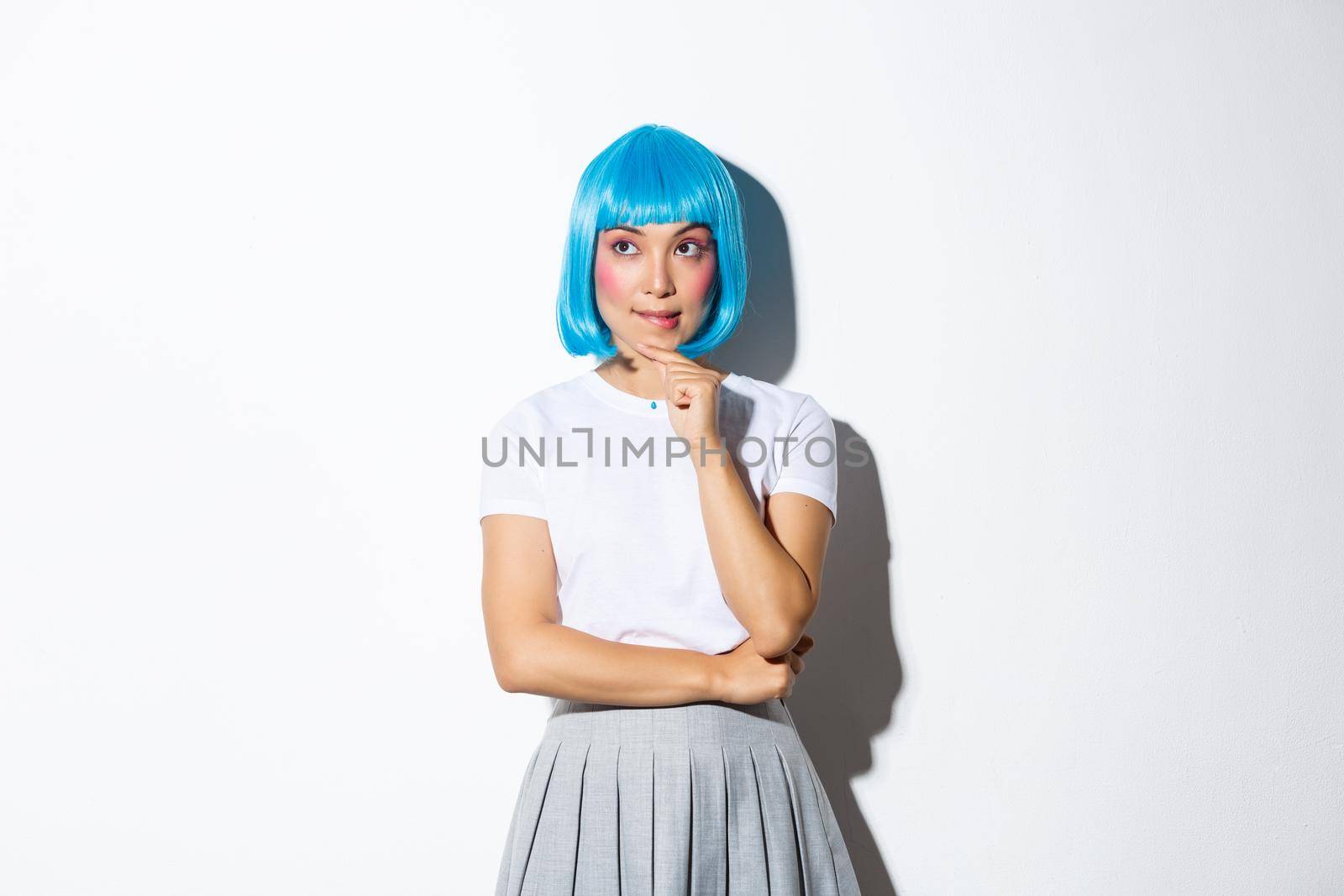 Image of thoughtful kawaii asian girl looking at upper left corner, thinking about something, standing in blue wig, dressed up for party or halloween.