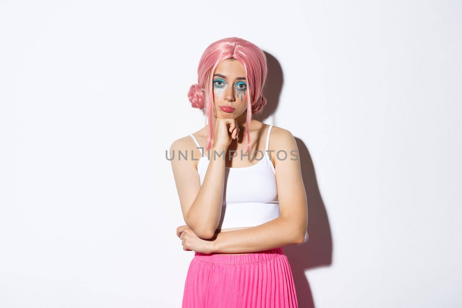 Portrait of sad reluctant girl standing in halloween costume and pink wig, looking bored or disappointed at camera.