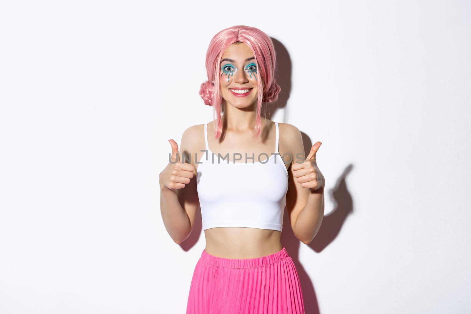 Portrait of satisfied smiling girl showing thumbs-up in approval, praise good choice, standing in halloween costume with pink with and bright makeup.