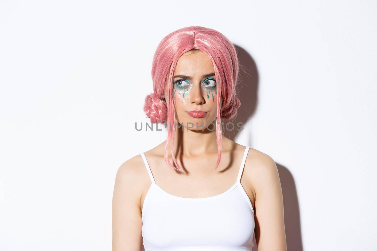 Close-up of confused cute girl in pink wig, grimacing and looking upper left corner with disappointed face, standing in halloween costume over white background by Benzoix