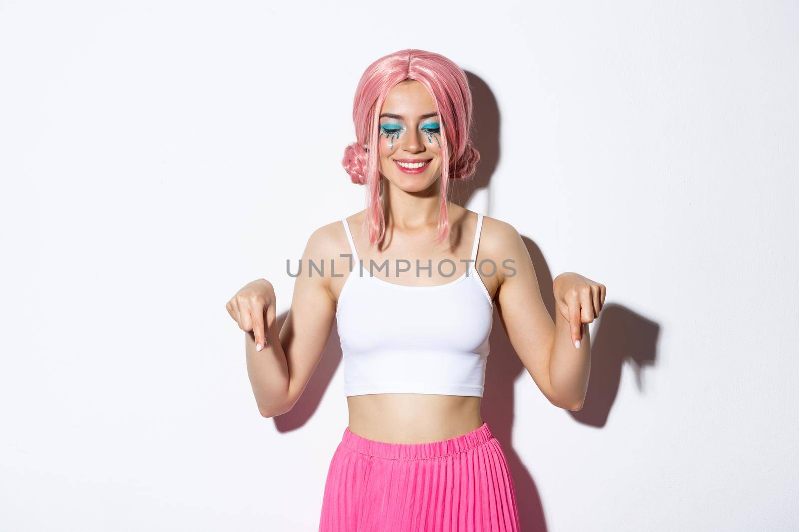 Happy smiling woman dressed for halloween party, celebrating holiday and pink wig and bright makeup, pointing fingers down at your logo by Benzoix