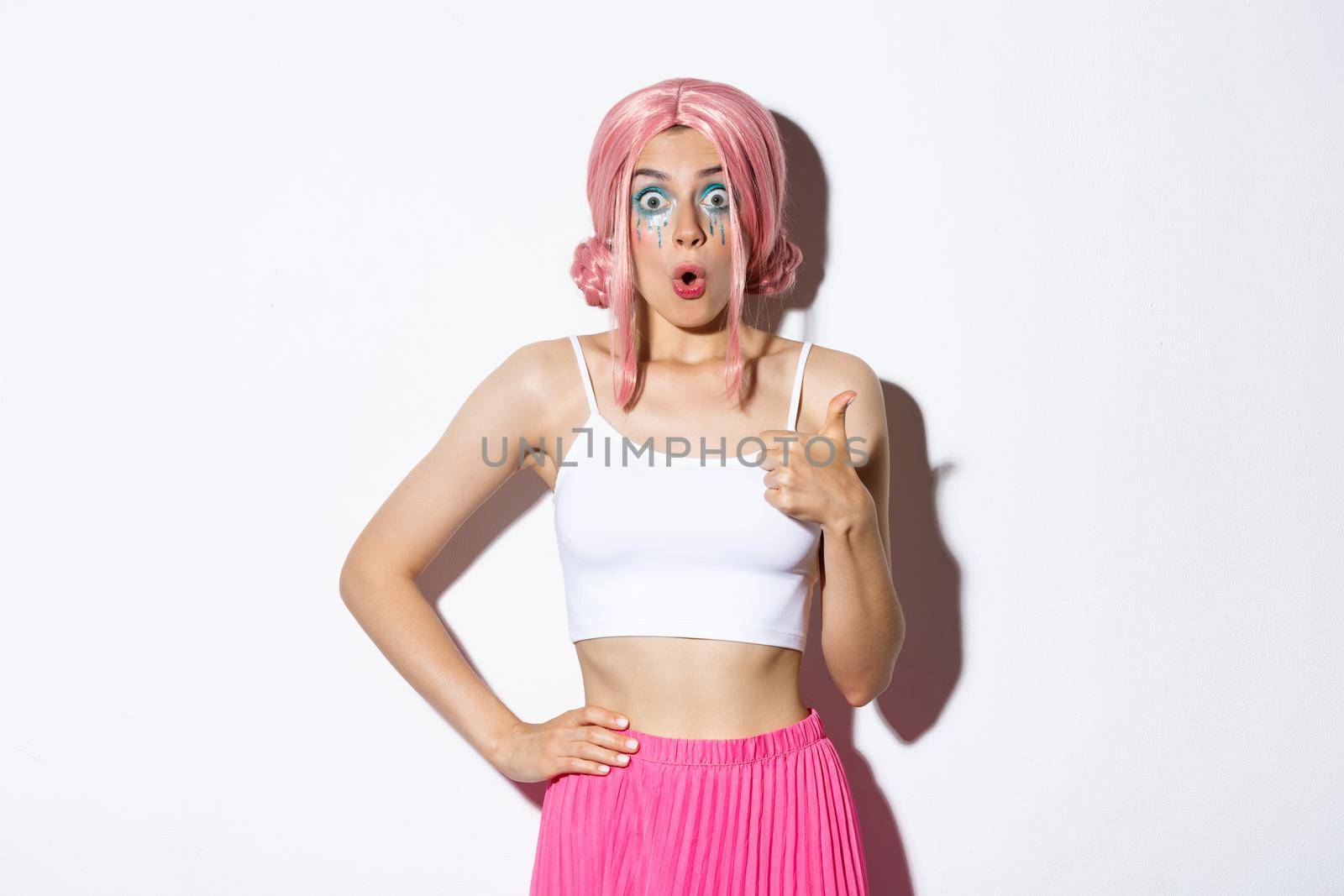 Portrait of impressed cute girl in party wig, looking amazed, showing thumbs-up in approval, like something good, standing over white background by Benzoix
