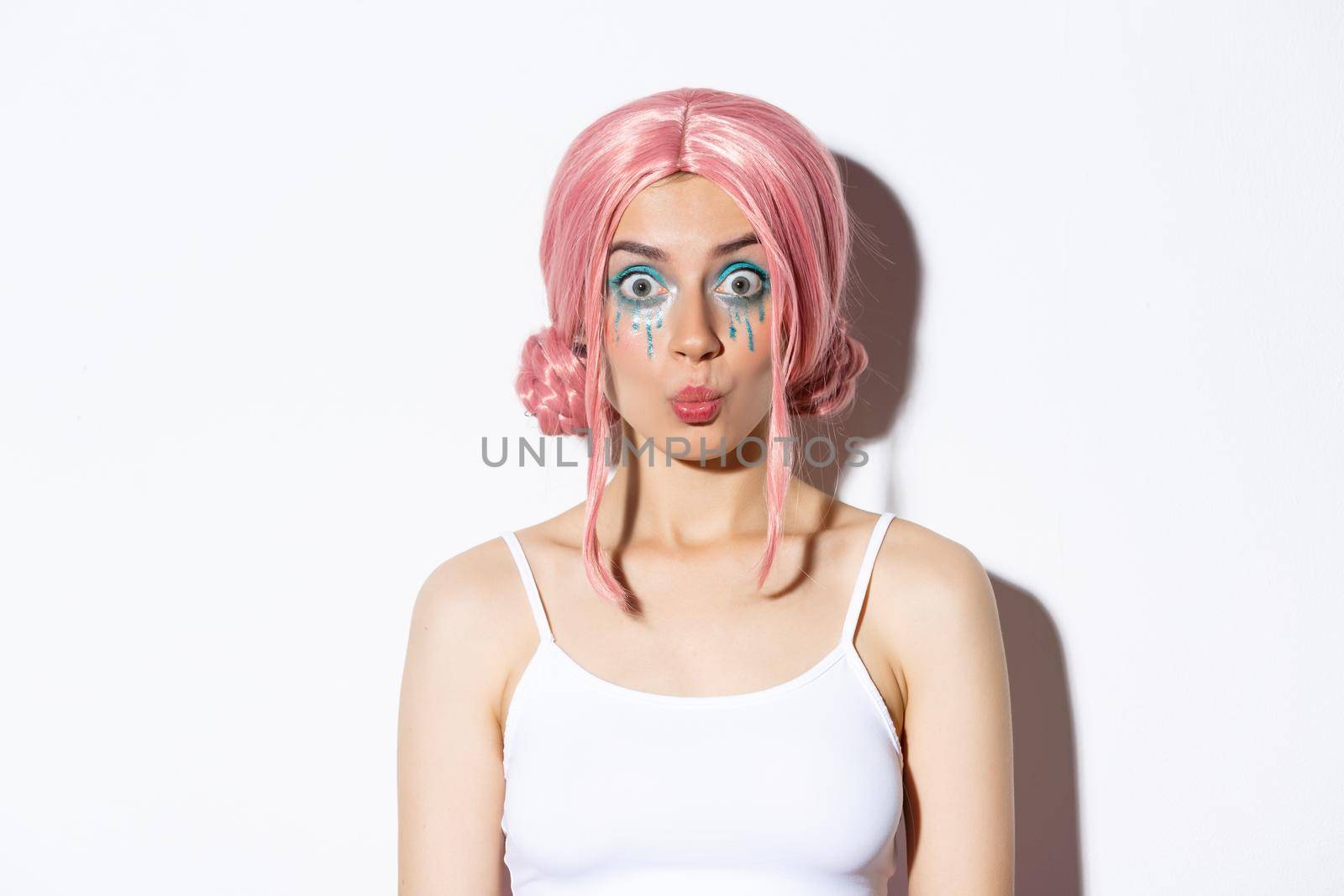 Close-up of surprised attractive girl in pink wig and fairy costume, looking amused, celebrating halloween, standing over white background.
