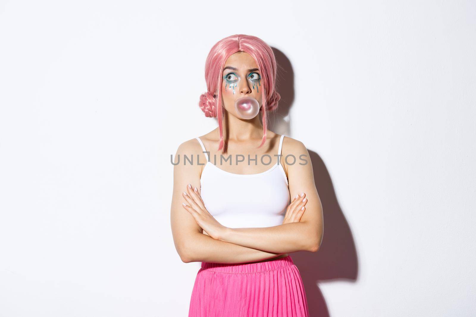 Image of confused party girl in pink wig, wigh bright makeup, blowing bubble gum and looking indecisive at upper left corner, standing over white background by Benzoix