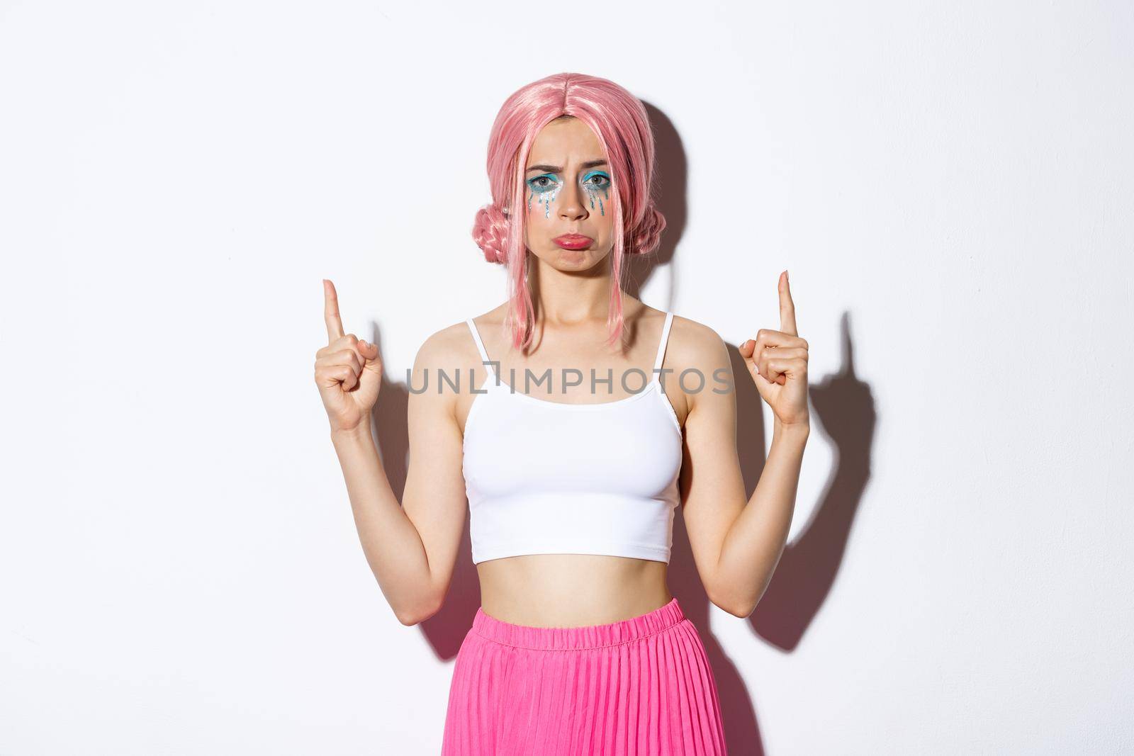 Portrait of disappointed silly girl in pink wig, pointing fingers up and sulking upset, complaining about something bad, standing over white background by Benzoix