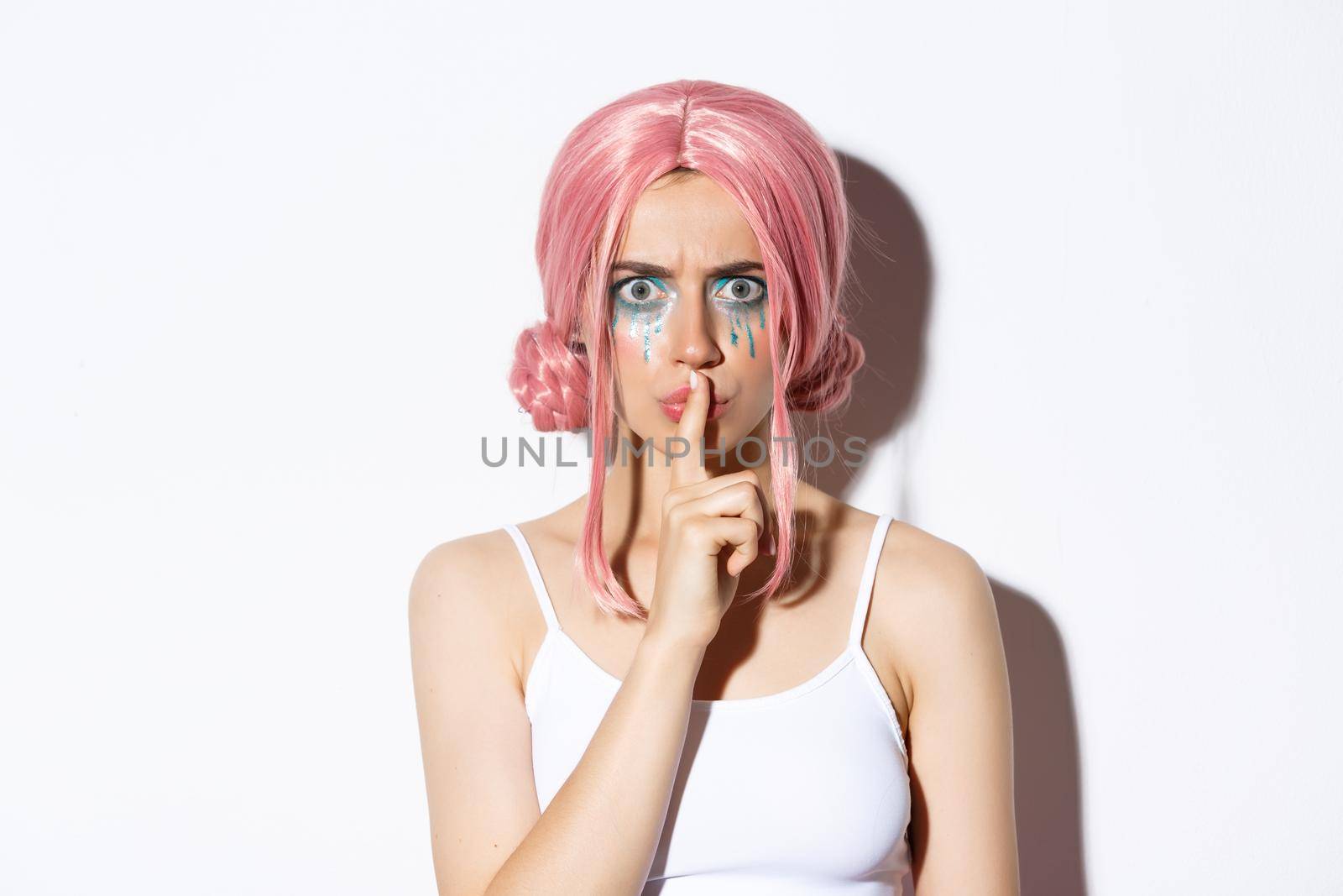 Close-up of angry girl with pink wig, frowning and shushing with mad face, standing over white background.