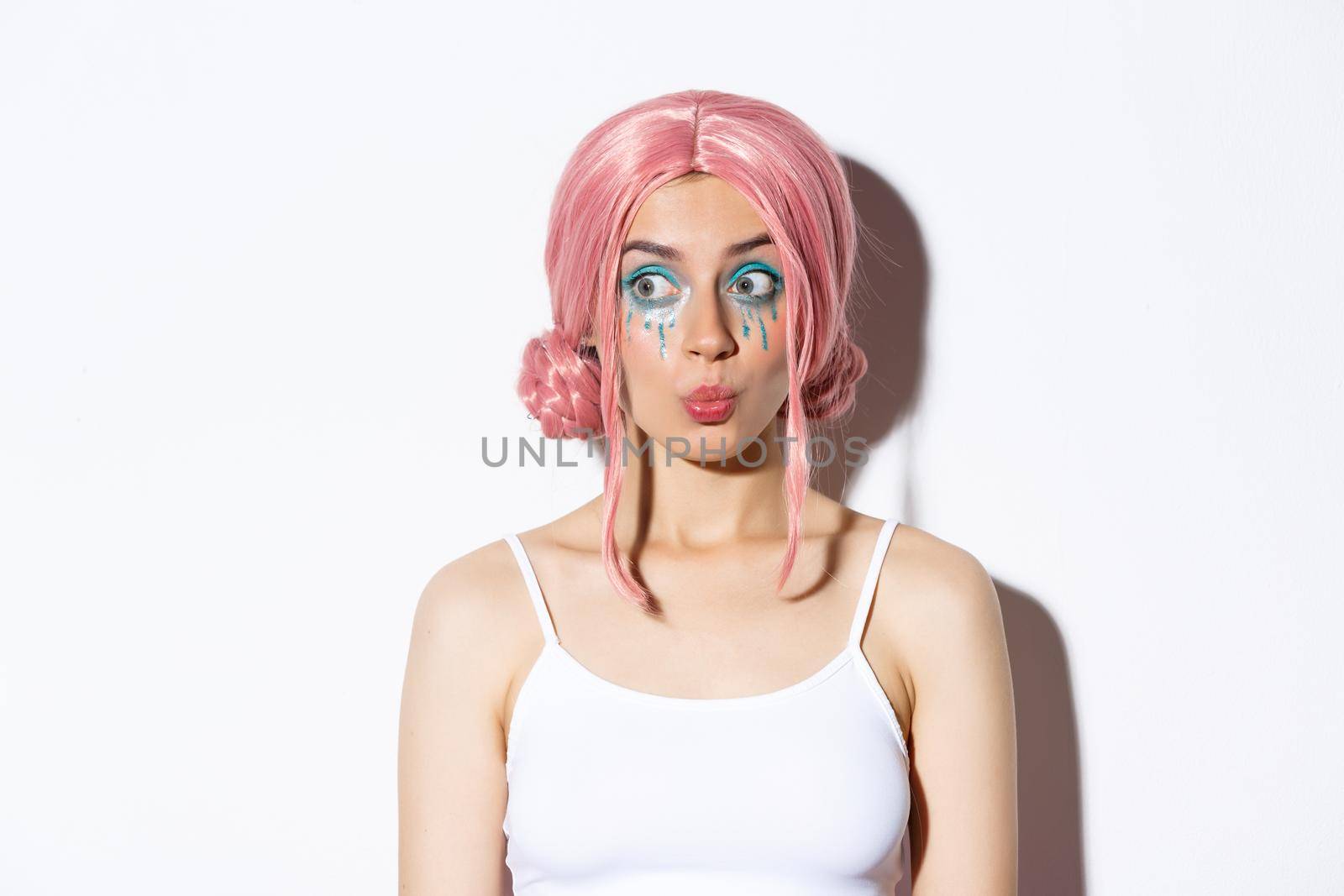 Image of beautiful silly girl in pink wig, with bright makeup, pouting and looking interested left, standing over white background by Benzoix