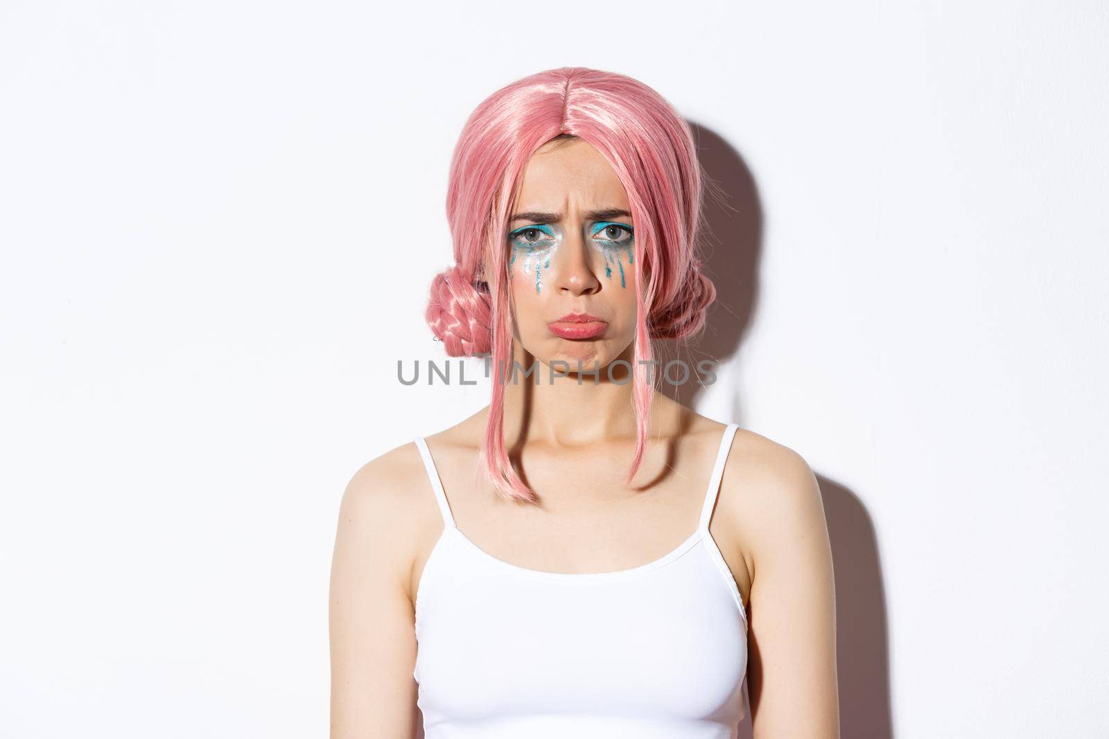 Close-up of sad disappointed girl in pink wig and halloween makeup, sulking offended, standing miserable over white background.