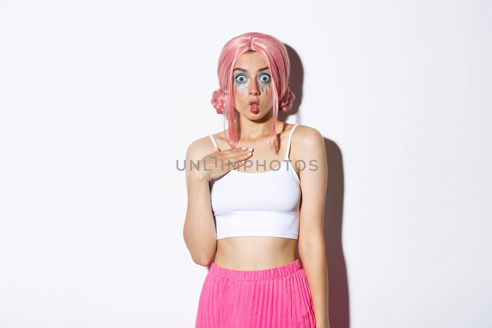 Image of silly pretty girl in pink wig, making surprised face and sucking lips, standing amazed over white background, celebrating halloween.
