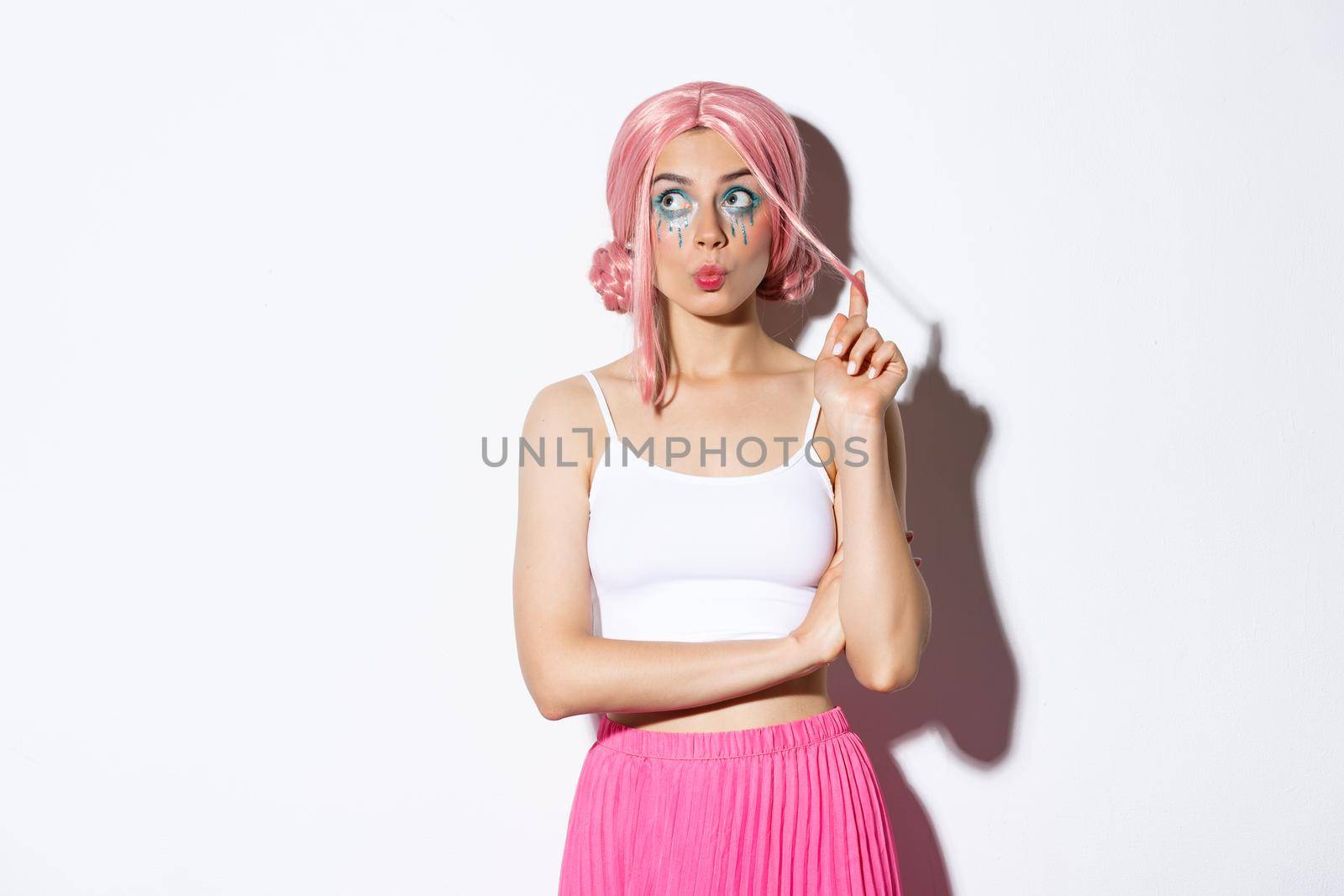 Silly young party girl in pink wig and halloween makeup, looking at upper left corner thoughtful, standing coquettish over white background by Benzoix
