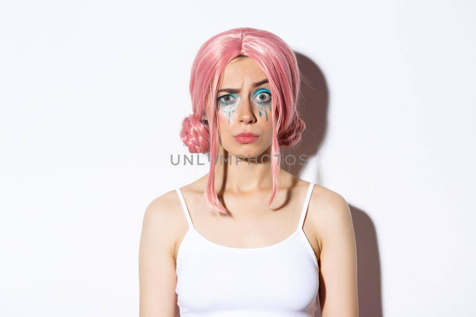 Close-up of confused girl in pink wig, raising eyebrow with suspicious expression, standing over white background.
