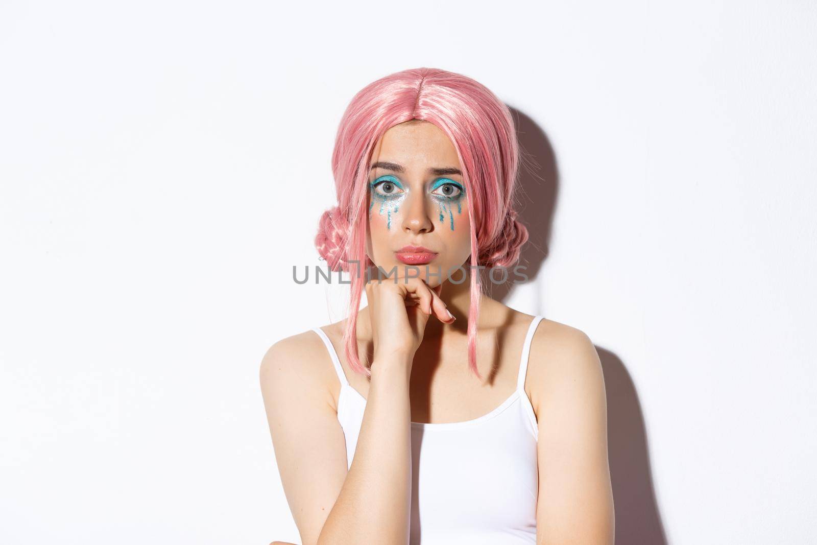 Close-up of sad cute girl with halloween makeup and pink wig looking upset, sulking while standing over white background by Benzoix