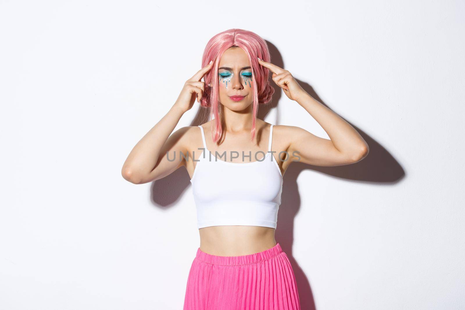 Portrait of distressed caucasian girl with pink wig and party makeup, standing with closed eyes and touching head, trying to think or remember something by Benzoix
