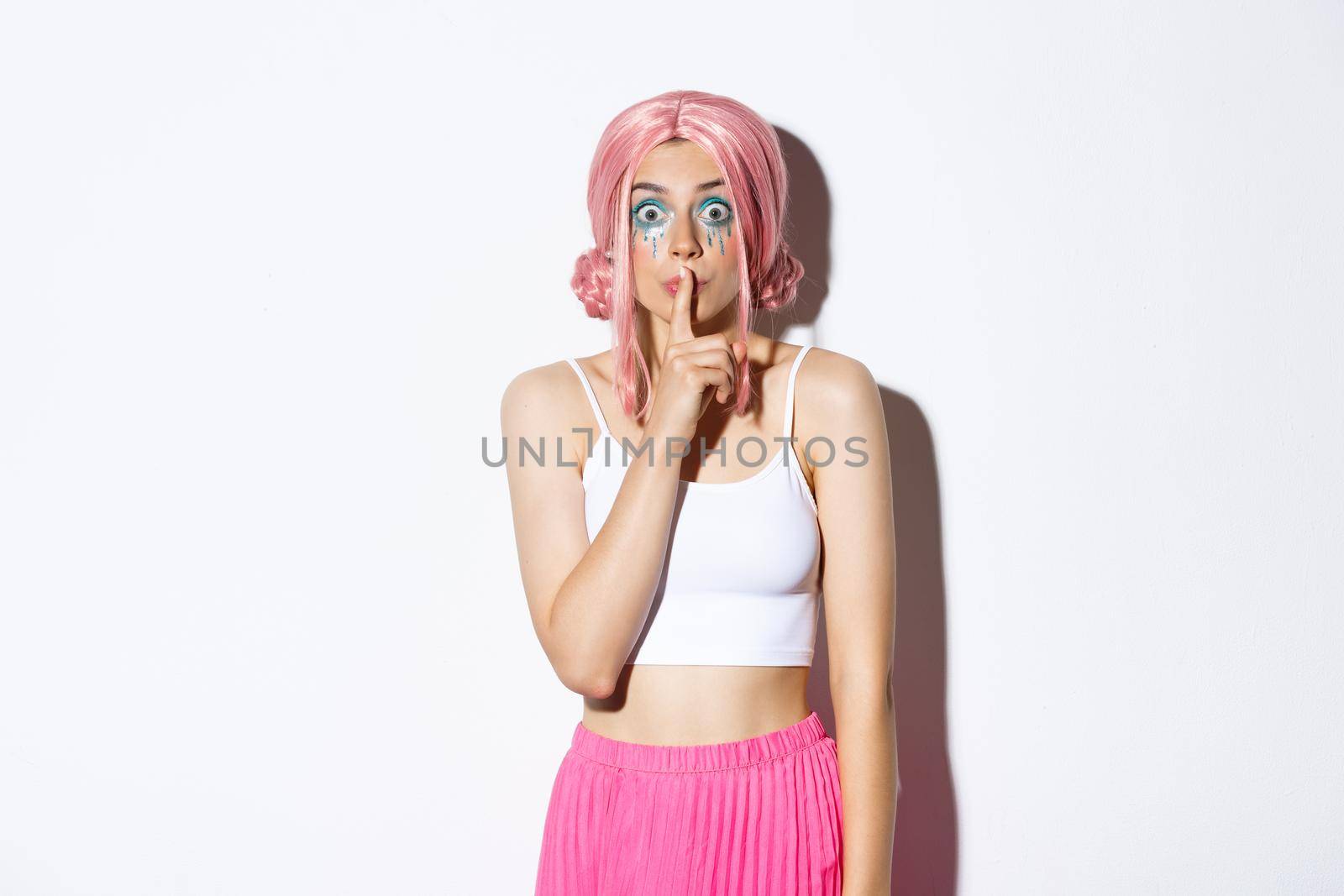 Worried attractive girl in pink anime hair and glitter, asking keep quiet, showing shush sign, press index finger to lips and looking concerned. Woman share a secret, standing over white background by Benzoix