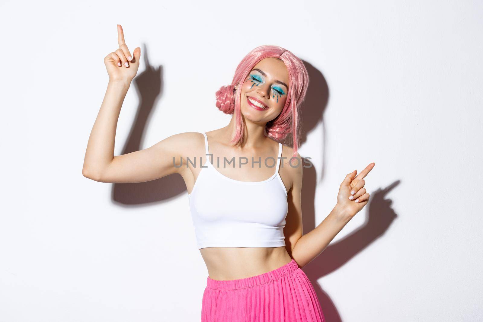 Portrait of happy beautiful girl having fun, dancing and smiling, celebrating holiday on party, wearing pink wig with bright makeup.