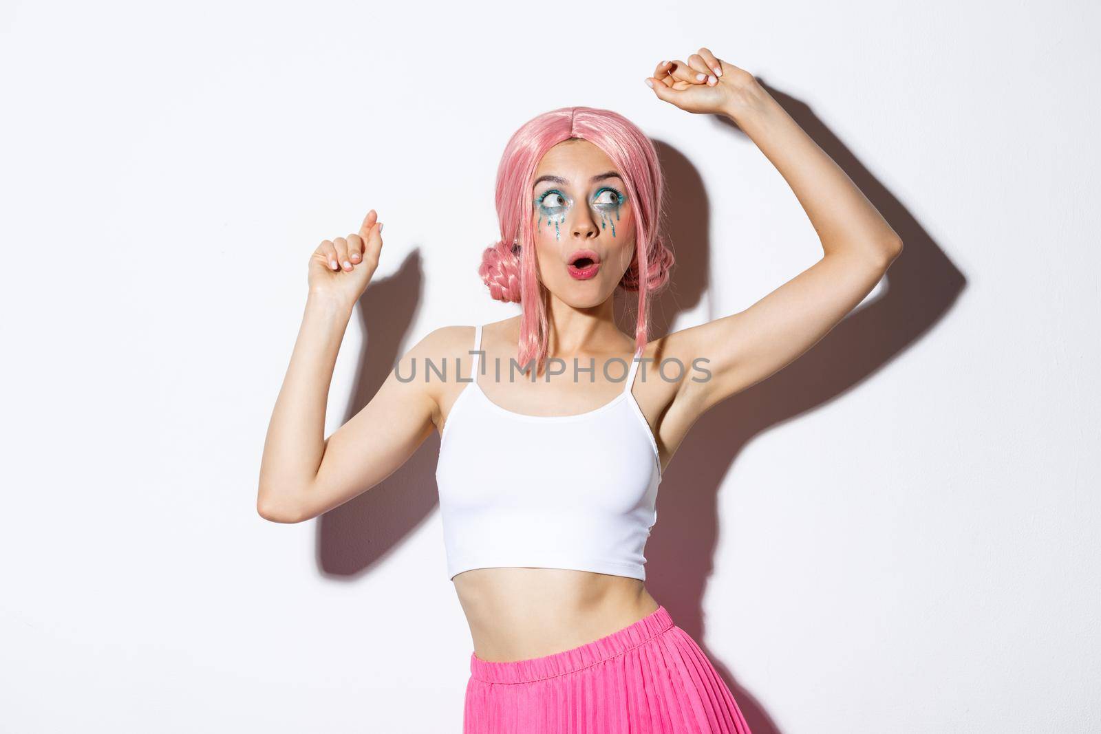 Image of attractive party girl with pink wig and bright makeup, having fun and celebrating holiday, dancing happy over white background.