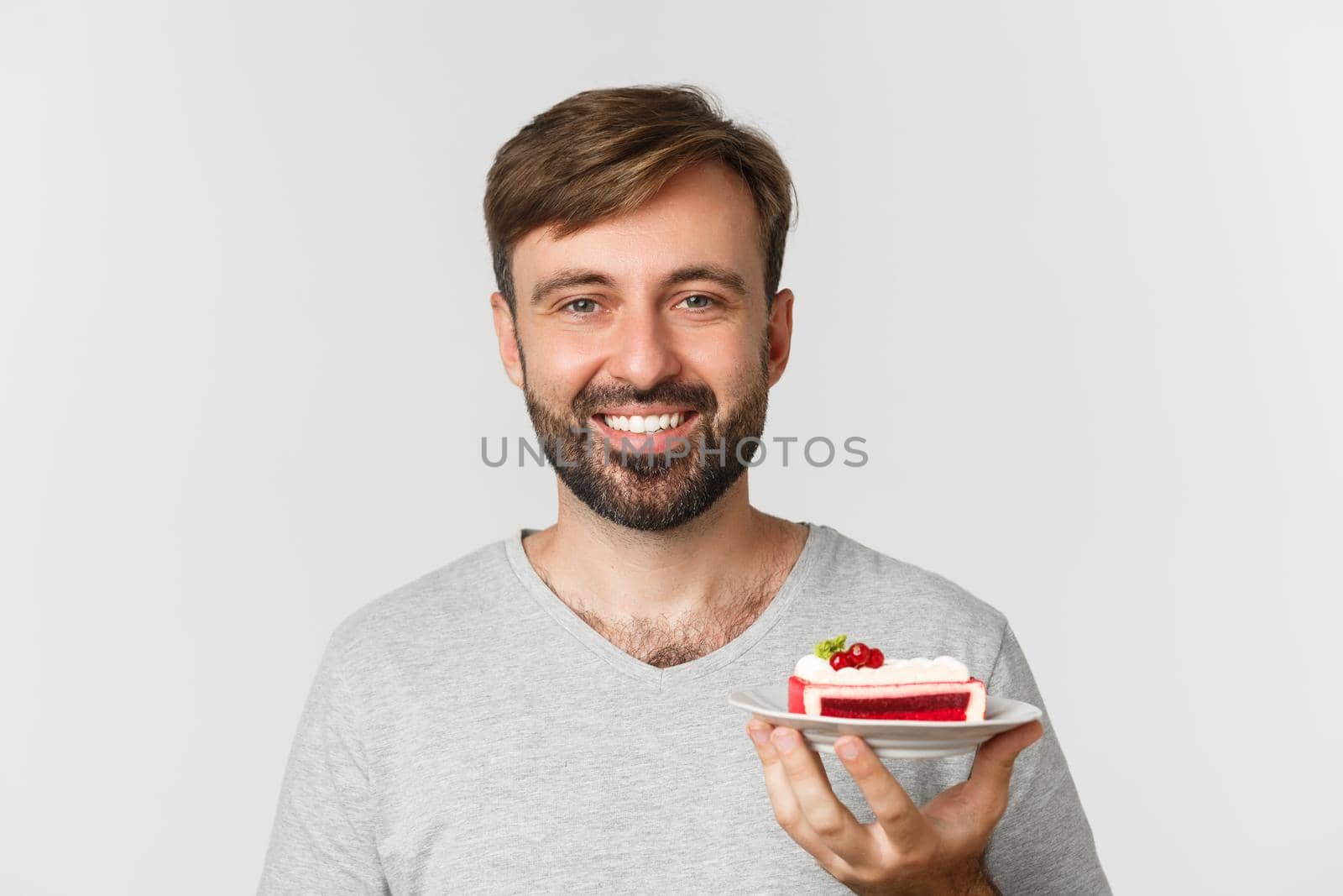 Close-up of handsome bearded man, smiling and holding cake, standing over white background by Benzoix