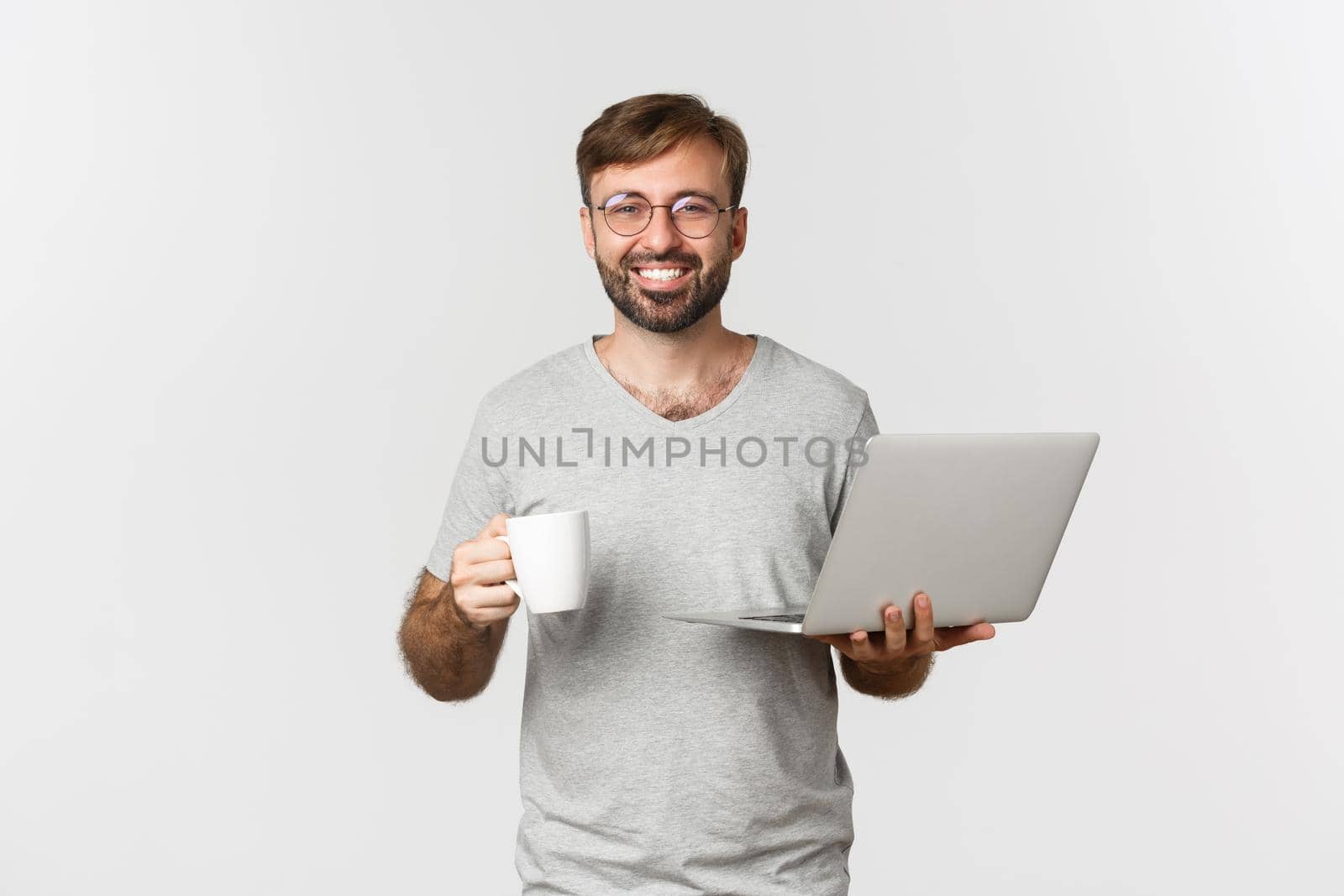 Young happy man working with laptop, drinking coffee and smiling, standing over white background.