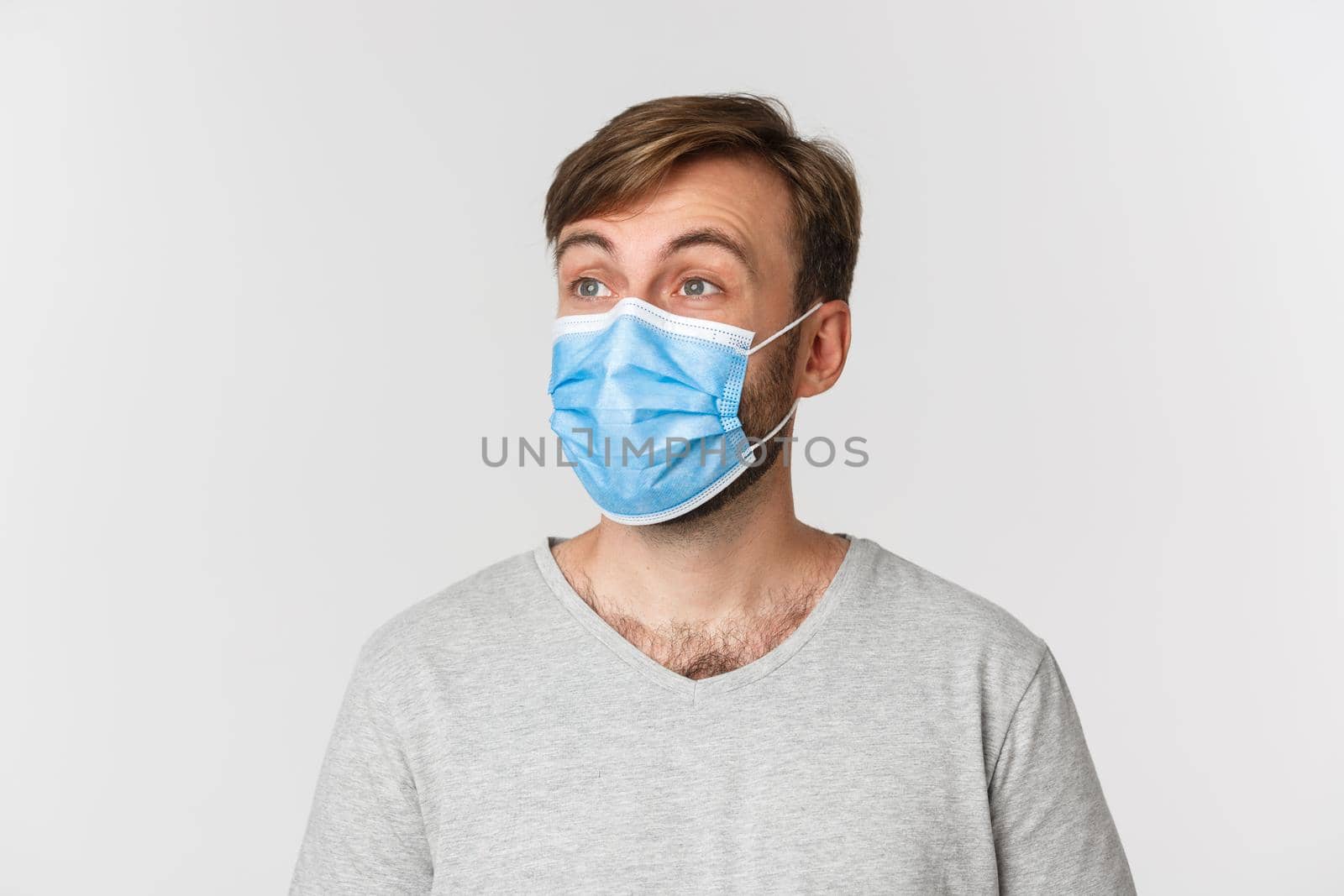 Concept of pandemic, covid-19 and social-distancing. Close-up of handsome man in medical mask, looking left at logo with surprised face, standing over white background.