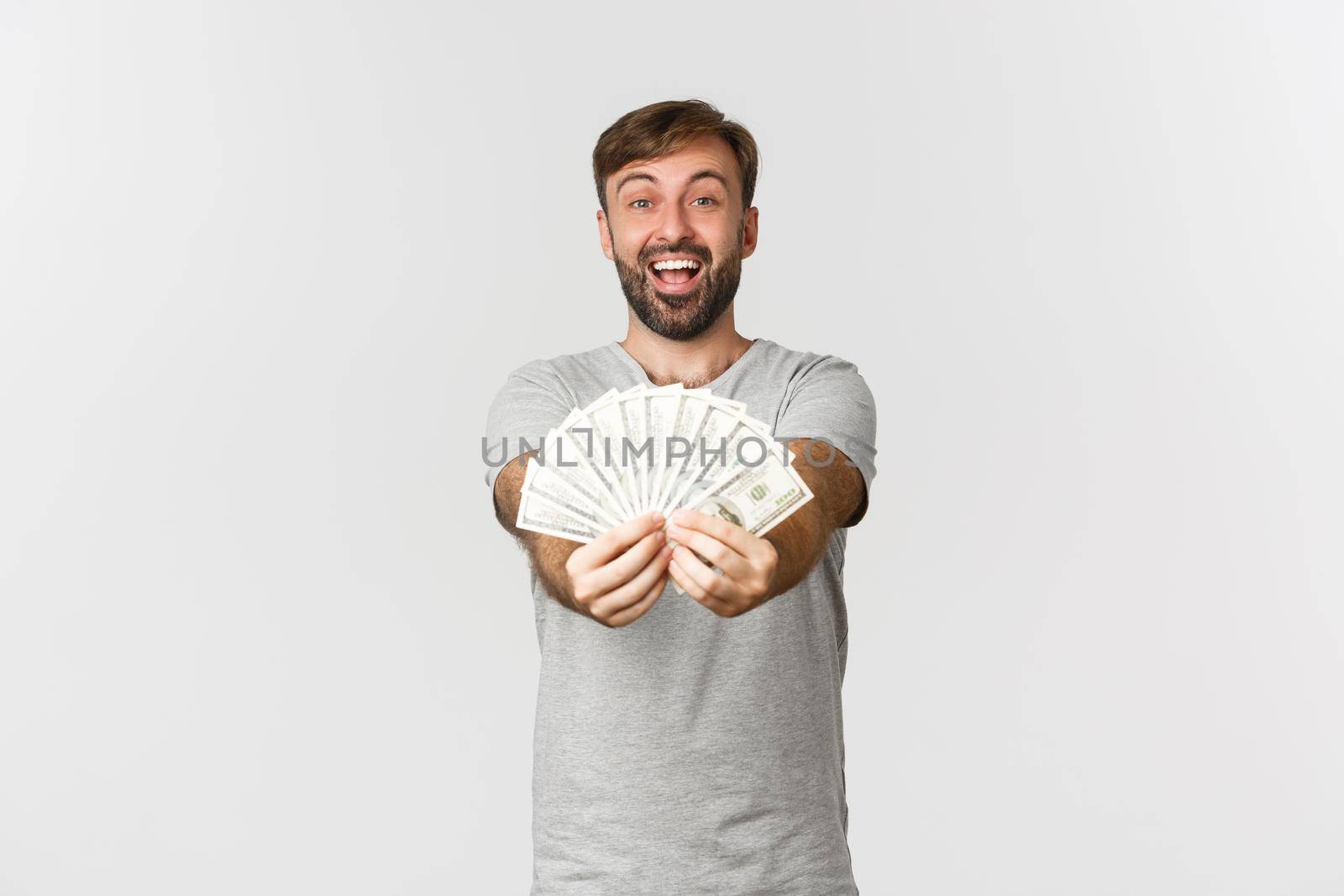 Image of happy caucasian guy with beard, giving you money and smiling, showing cash, standing over white background.