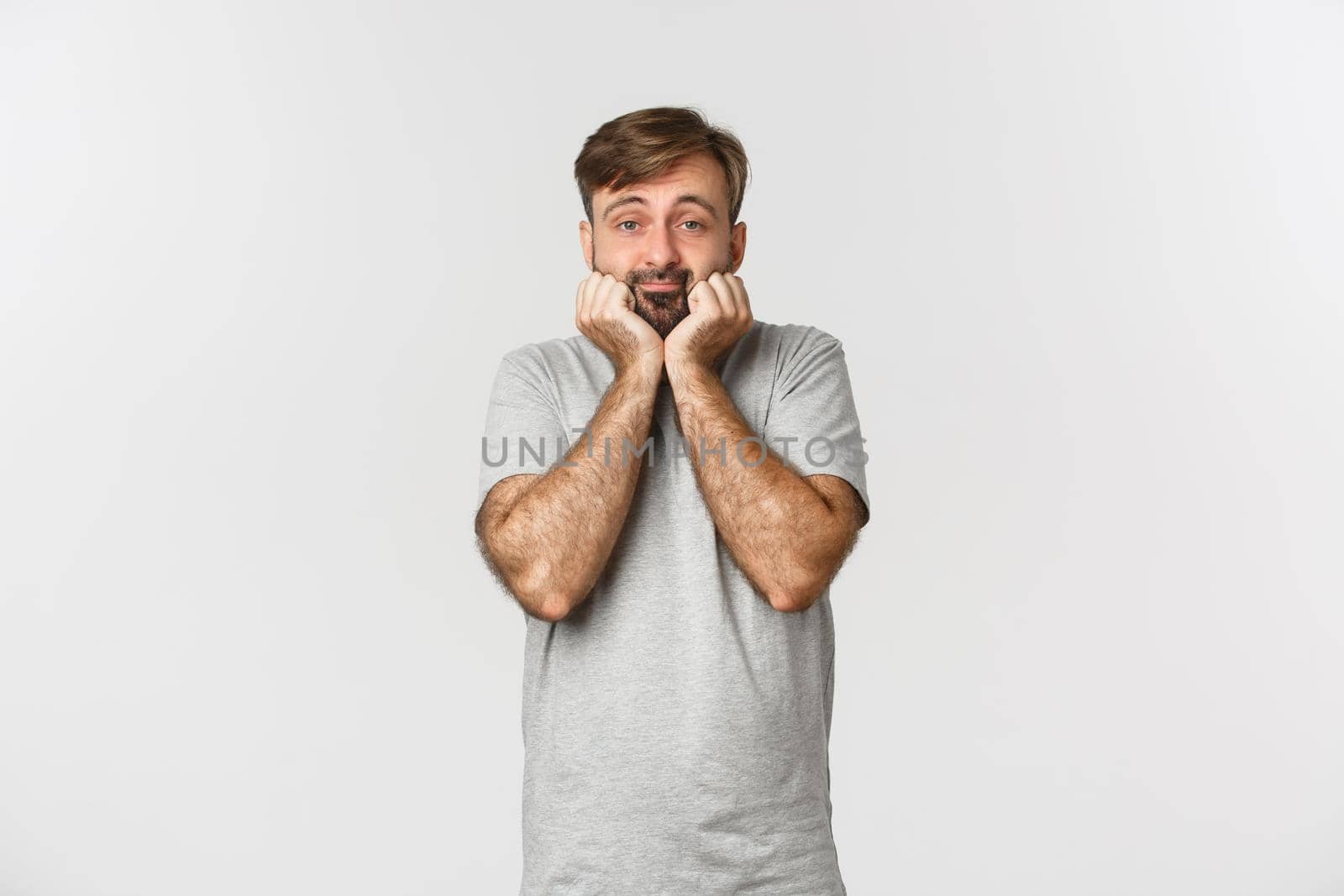 Portrait of cute and silly adult man with beard, leaning on palm and looking at camera silly, standing over white background.