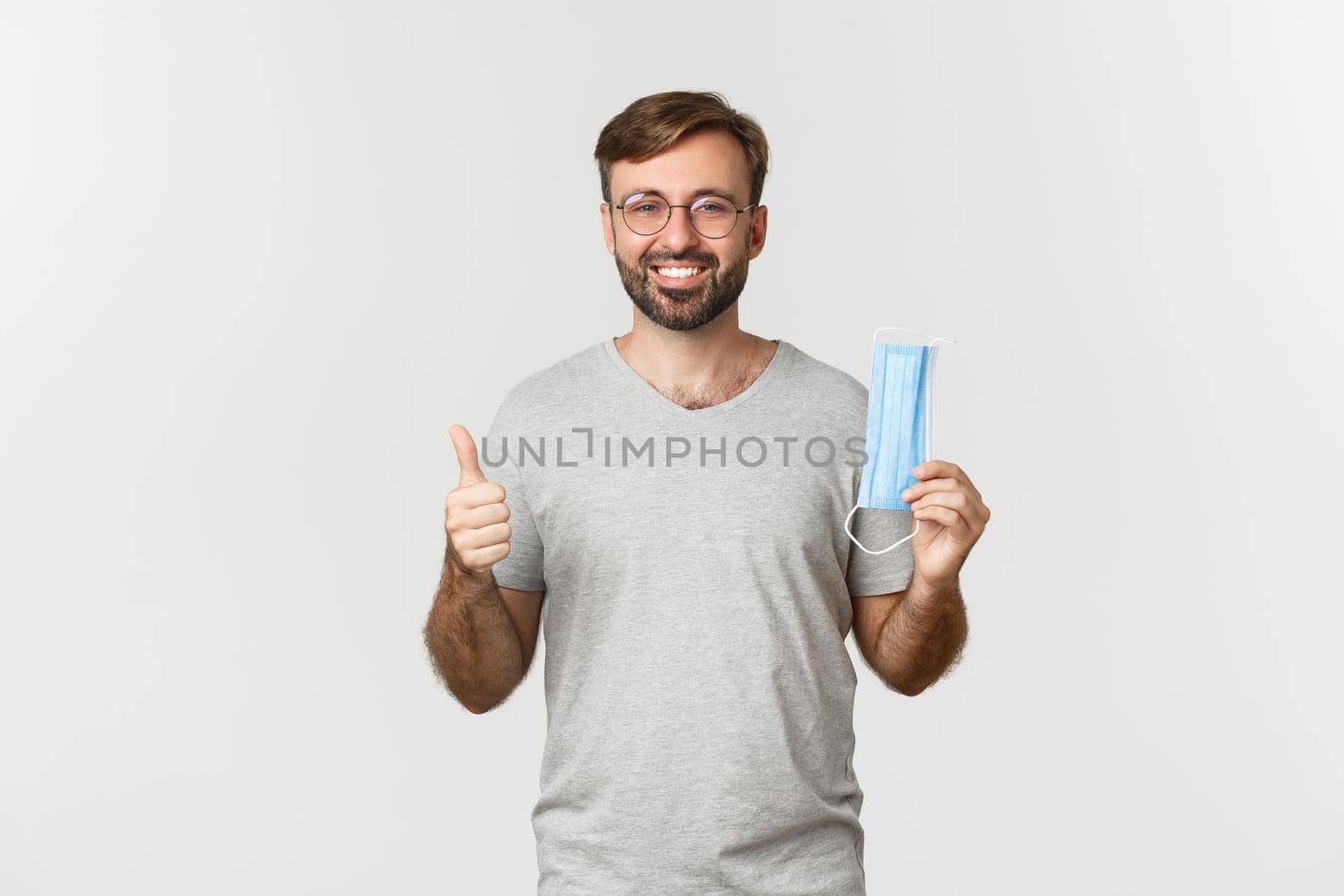 Concept of pandemic, coronavirus and social-distancing. Image of handsome smiling guy in glasses, showing thumbs-up and recommending to wear medical mask.