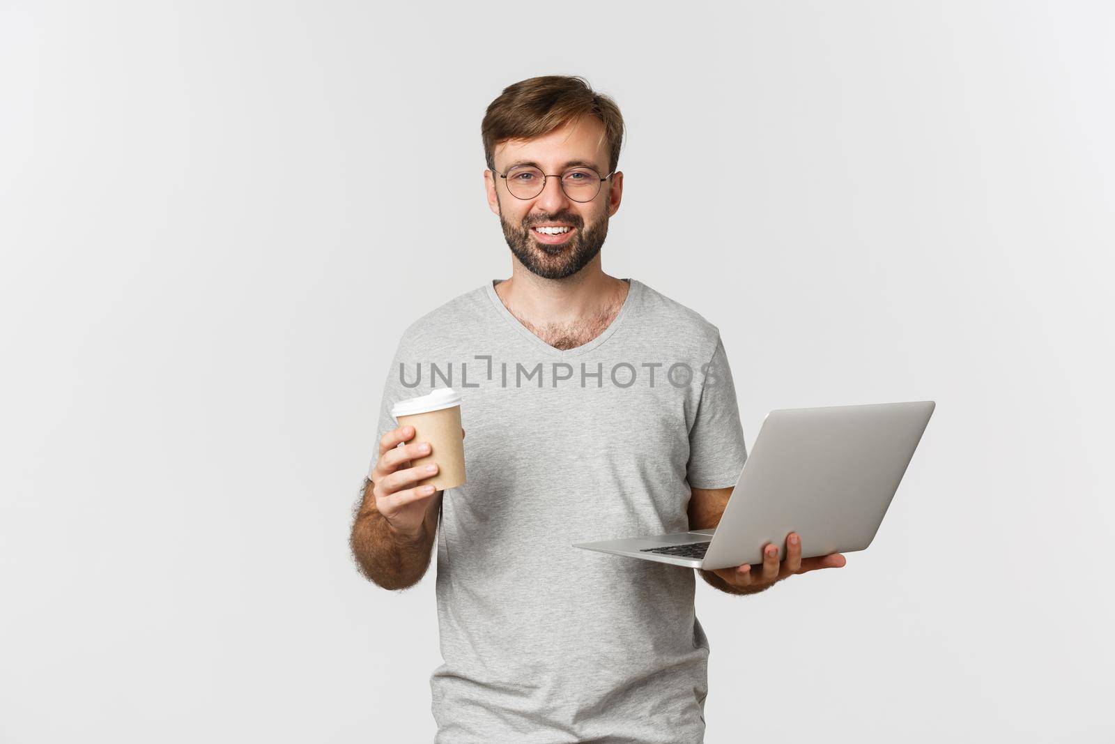 Portrait of handsome male freelancer, drinking coffee and working with laptop, standing over white background.