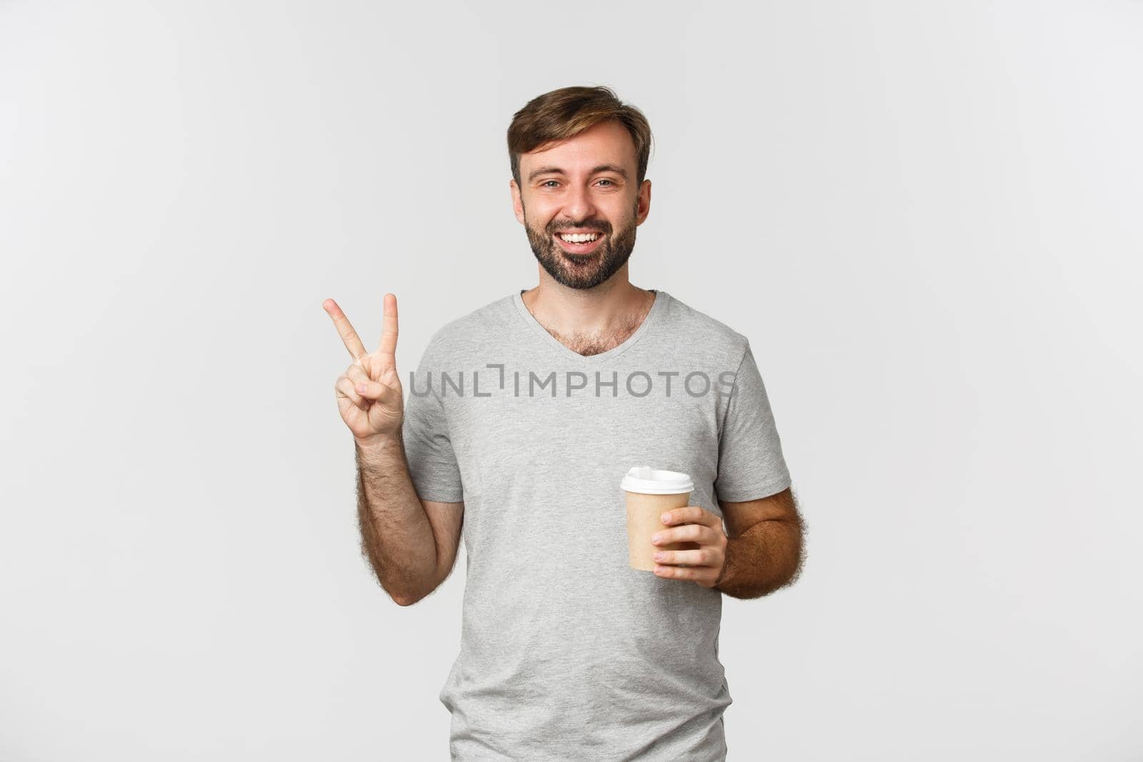 Image of happy guy drinking takeaway coffee, showing peace sign and smiling, standing over white background.