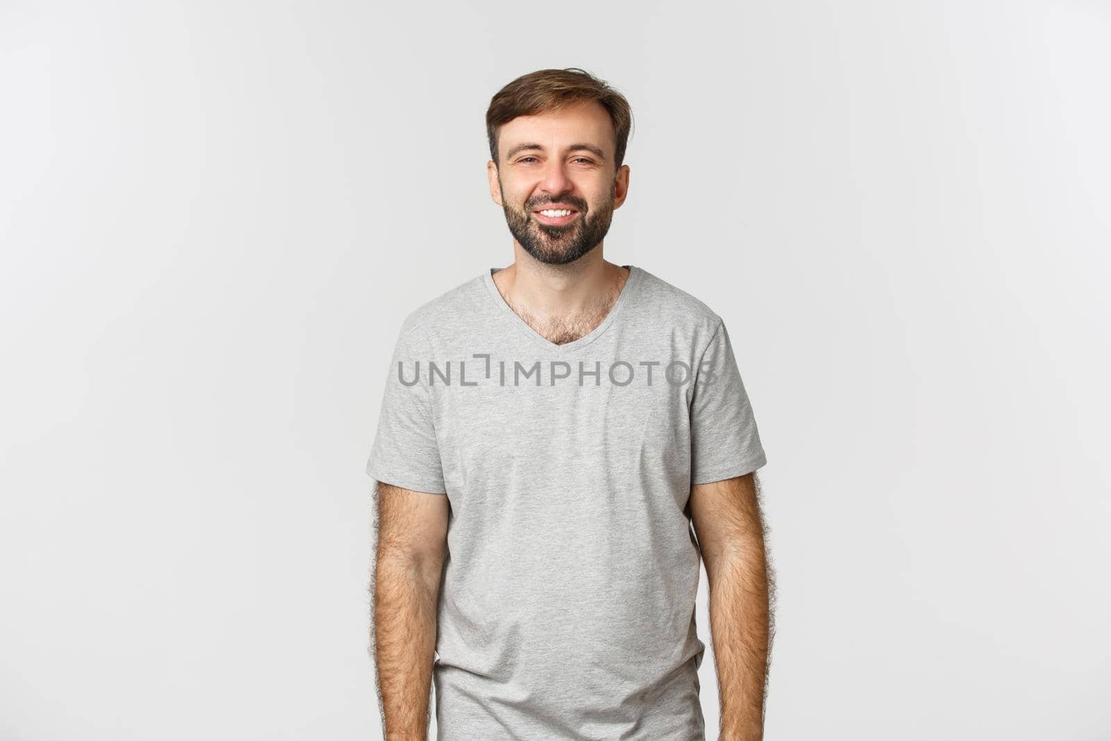 Handsome caucasian guy with beard, standing in grey basic t-shirt and smiling happy.